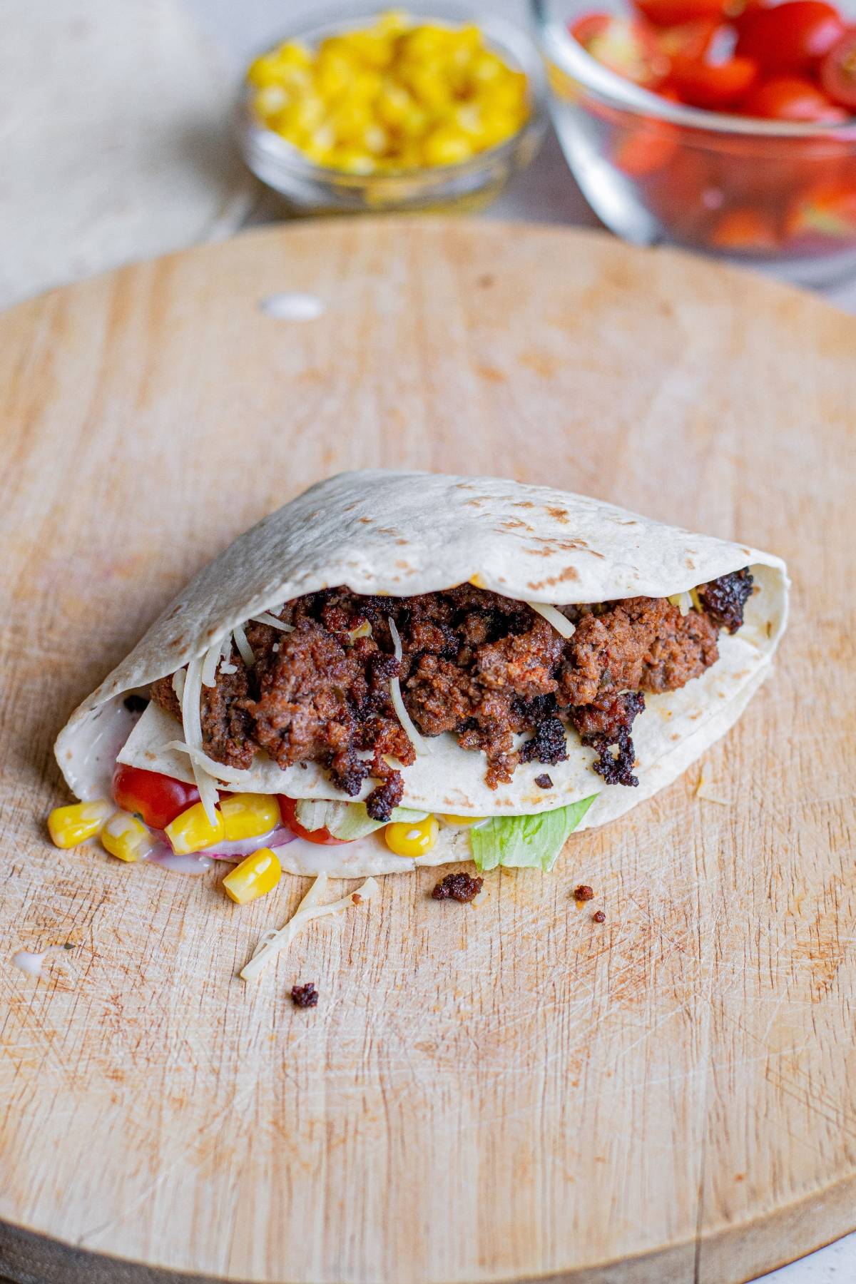A taco with ground meat, corn, lettuce, and tomato on a wooden board, inspired by the TikTok folded tortilla hack, with bowls of corn and tomatoes nearby.