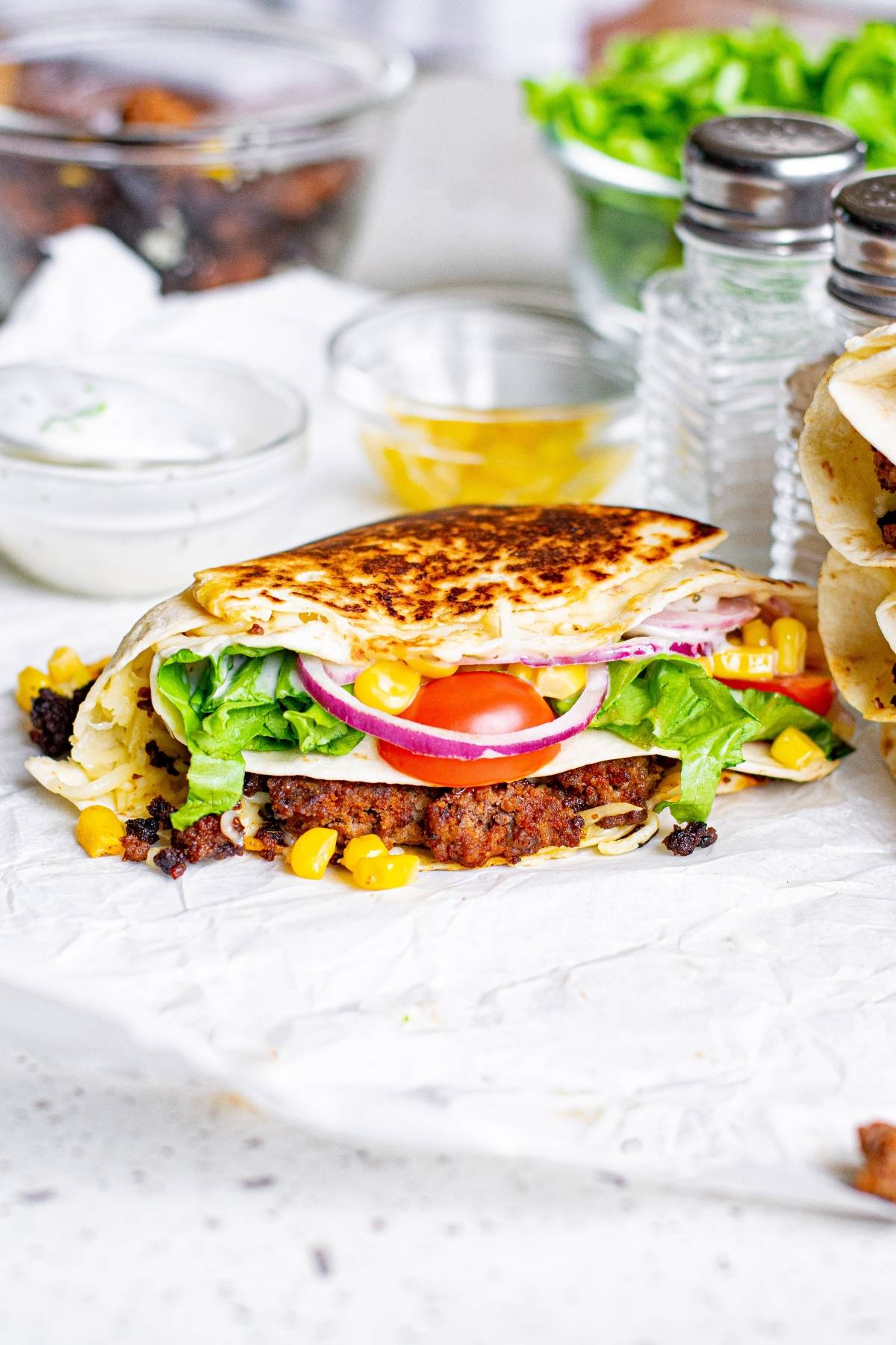 A folded tortilla hack featuring lettuce, tomato, onions, corn, and ground meat on parchment paper for a tasty crunchy beef tortilla folded wrap.