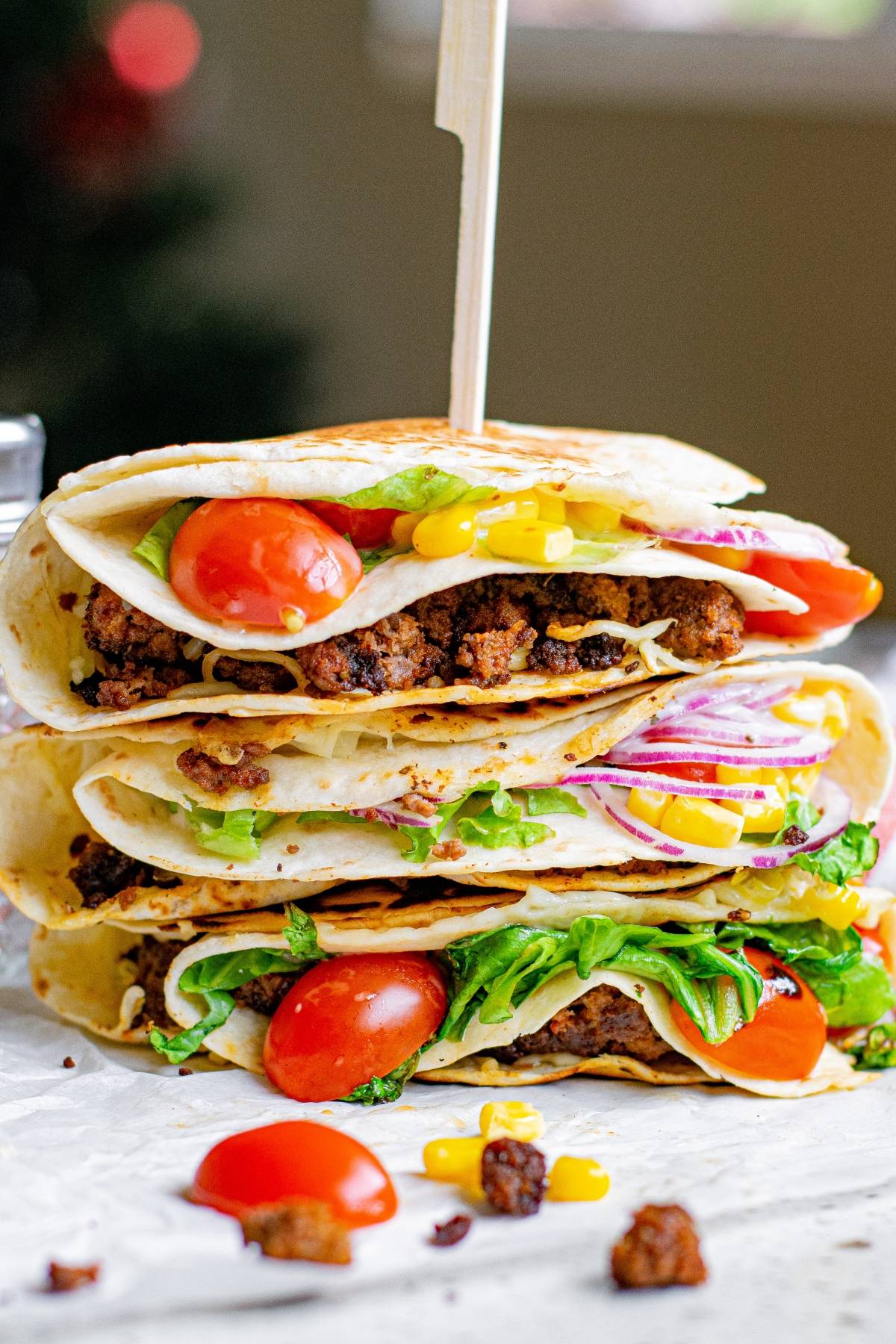 Three folded tacos stacked and held by a skewer, each made with the popular TikTok tortilla hack—crunchy beef tortilla folded wraps packed with lettuce, tomatoes, onions, and corn.