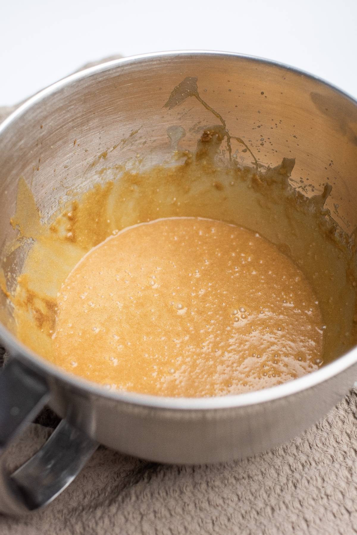 Thick, light brown batter mixture in a metal mixing bowl on a textured beige cloth, perfect for making delicious blonde brownies or blondie bars.