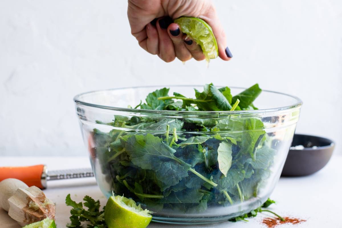 A hand squeezes a lime over a glass bowl filled with fresh leafy greens, prepping them for a Mexican inspired salad with a spicy yogurt lime dressing.