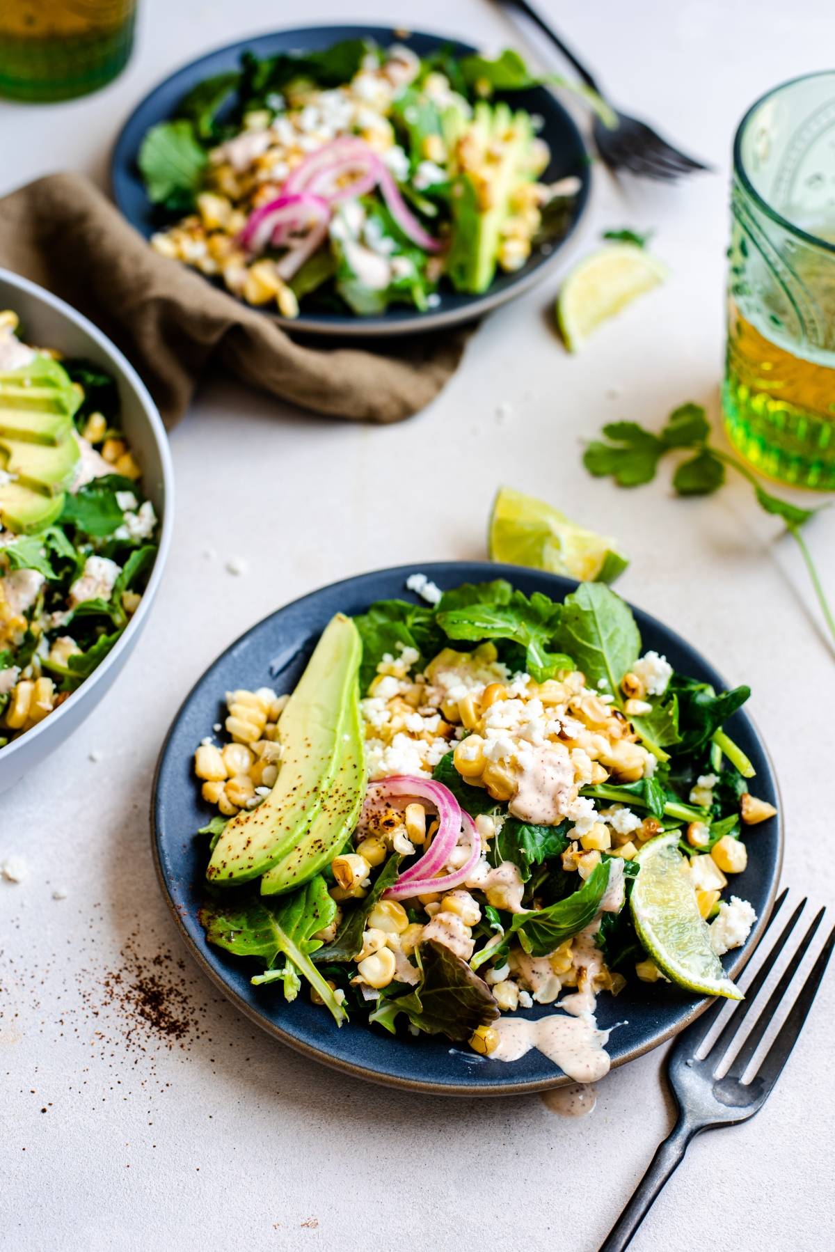 A plate of Mexican inspired salad with avocado, corn, greens, pickled onions, cheese, and a lime wedge, served next to a fork. Enjoy it with a zesty spicy yogurt lime dressing for an extra burst of flavor.