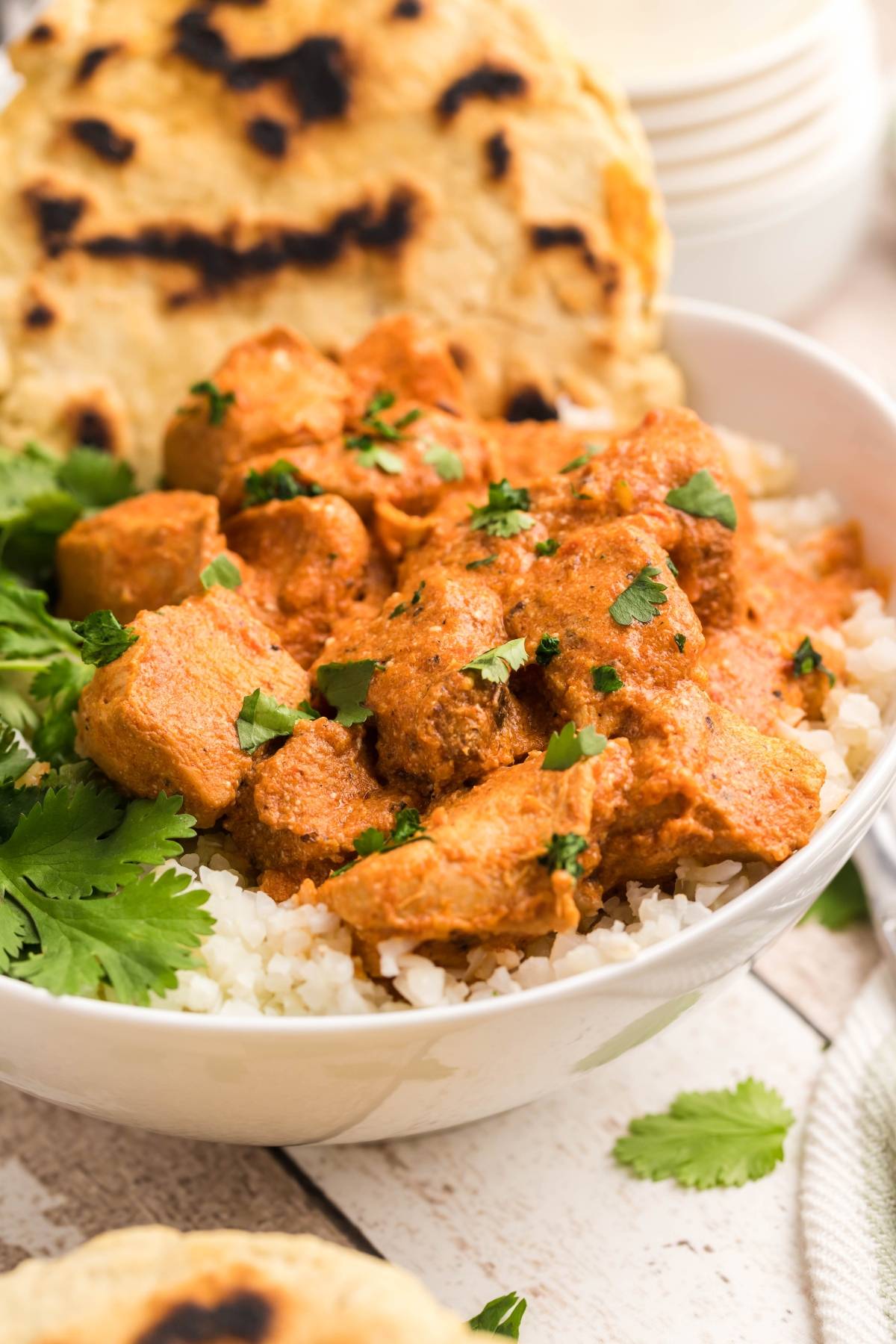 A bowl of rice topped with creamy chicken curry, garnished with cilantro, served with fluffy naan bread.