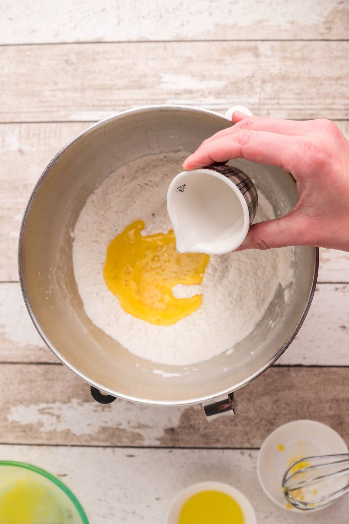 A hand pours milk into a mixing bowl with flour and a cracked egg on a wooden surface, preparing an easy naan recipe—perfect for making delicious no yeast naan bread at home.