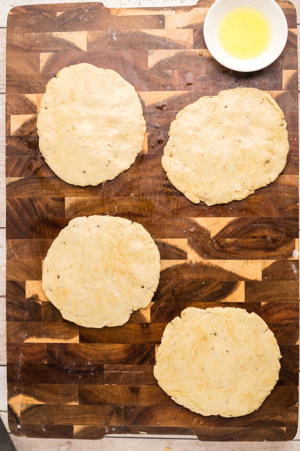 Four rounds of no yeast naan bread on a wooden board with a small bowl of oil in the corner—a perfect, easy naan recipe for your next meal.