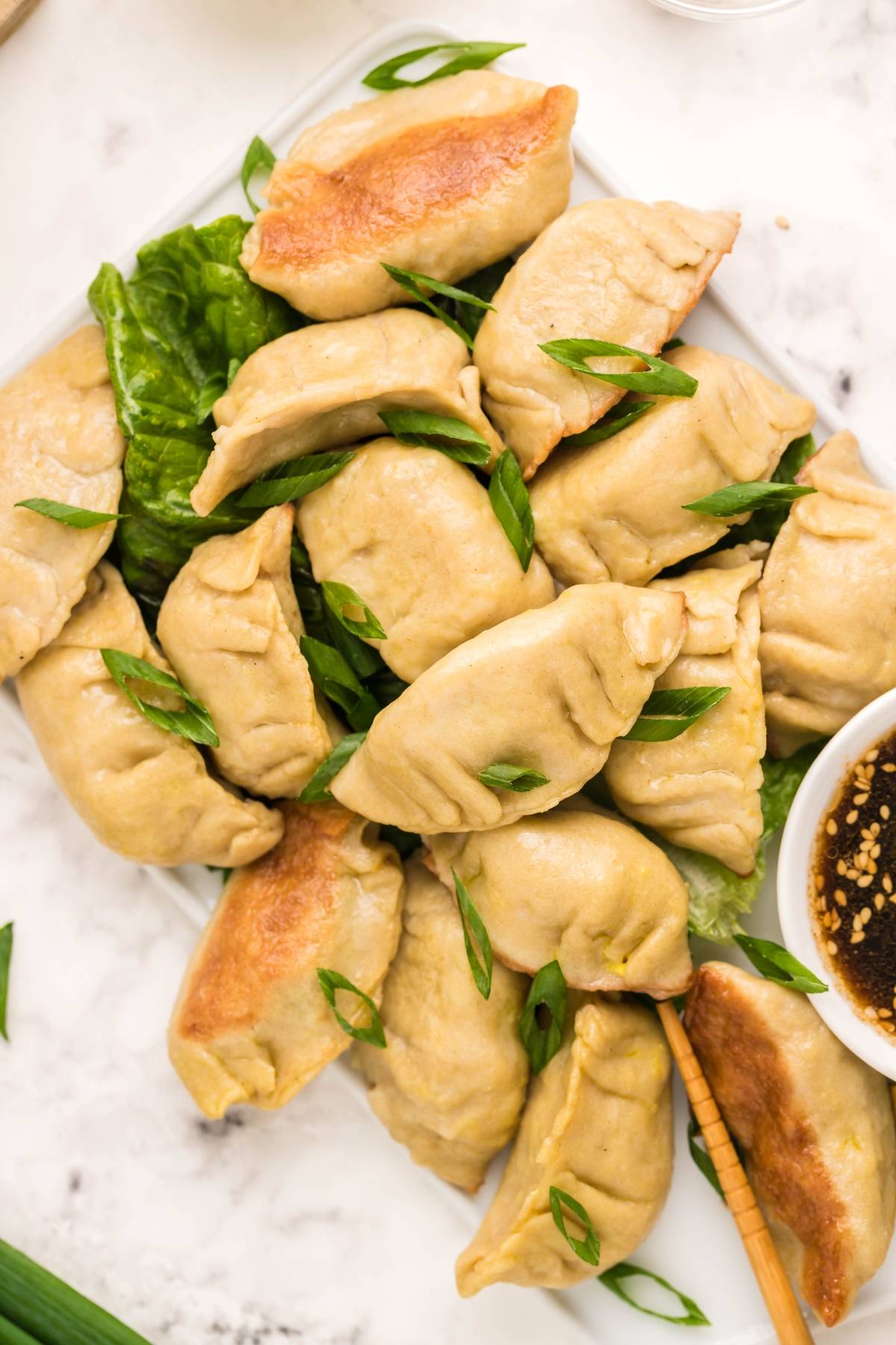 A plate of gluten free potstickers, pan-fried to perfection and garnished with sliced green onions, served with a flavorful dipping sauce.