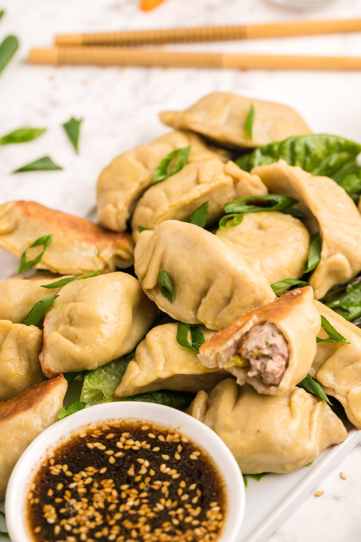A plate of gluten free potstickers with green onions, served with soy dipping sauce and chopsticks nearby.