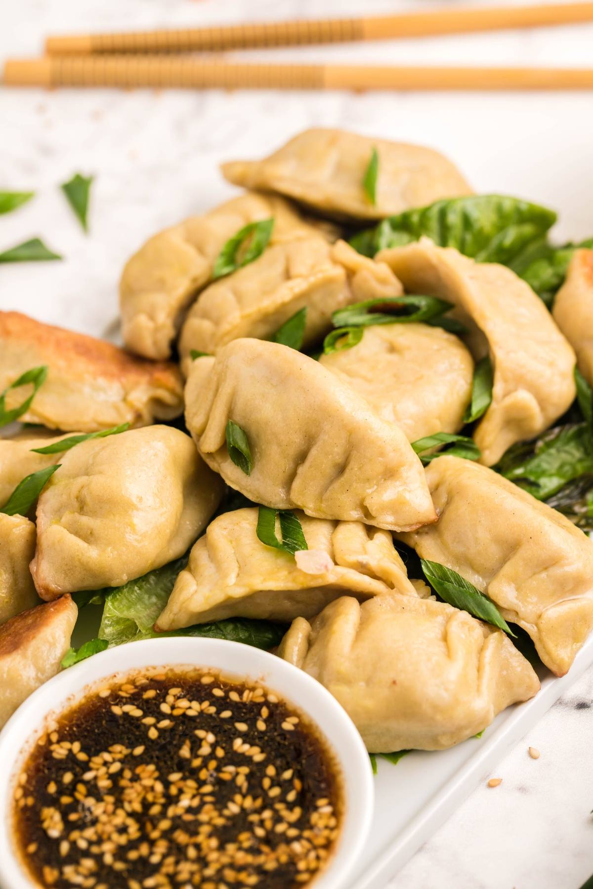 A plate of gluten free potstickers garnished with green onions, served with a bowl of soy dipping sauce and chopsticks.