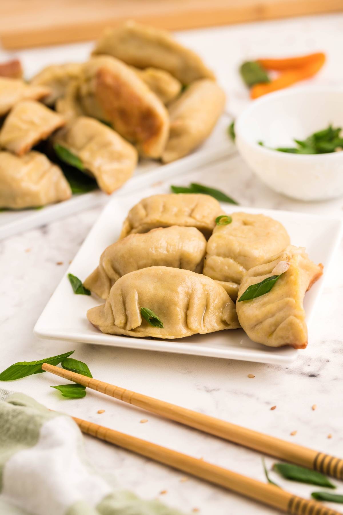 A plate of gluten free potstickers garnished with herbs, with chopsticks and more dumplings in the background.