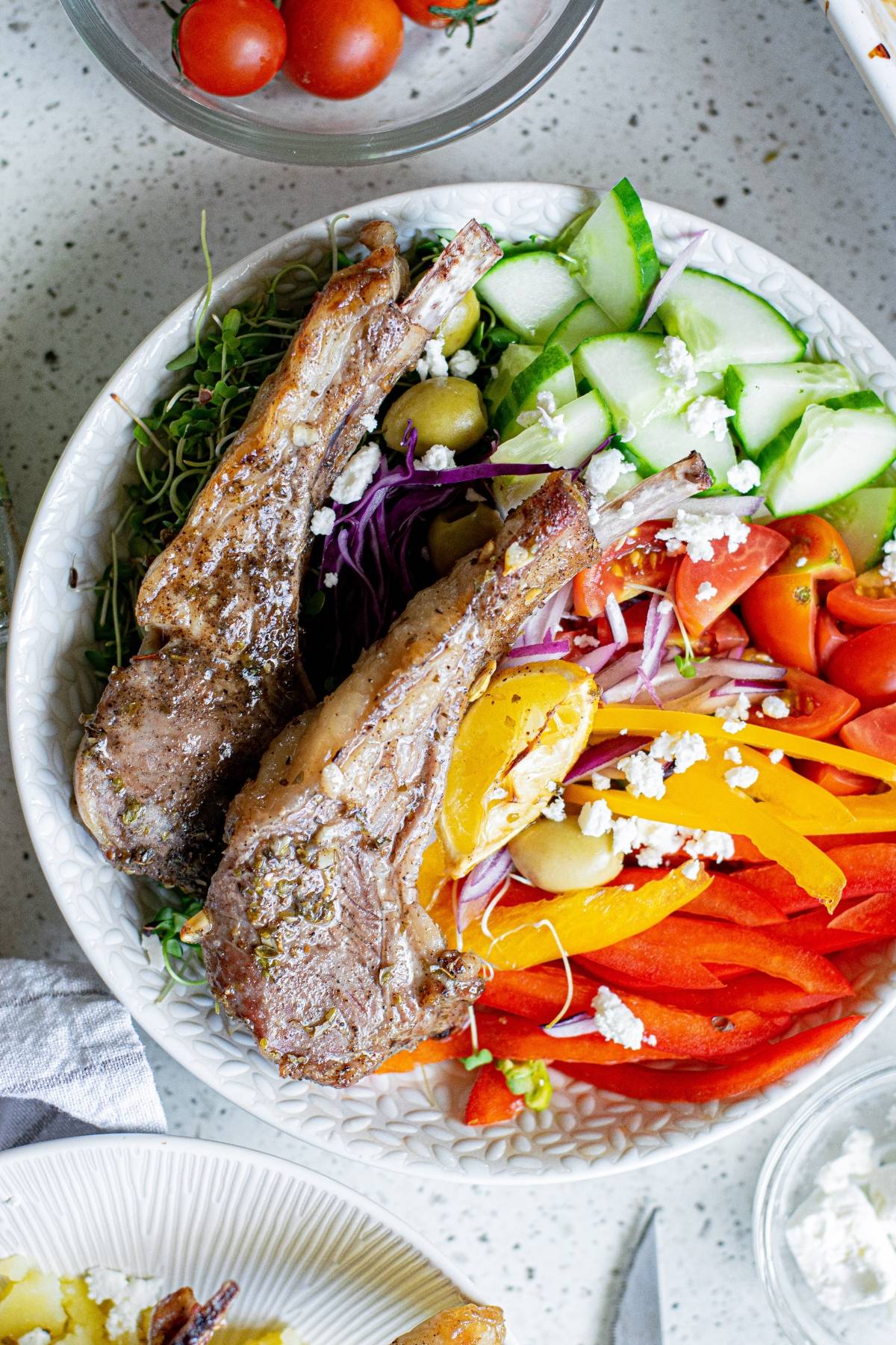 A bowl with Greek lemon baked pork chops, sliced cucumbers, peppers, tomatoes, olives, and crumbled feta cheese.