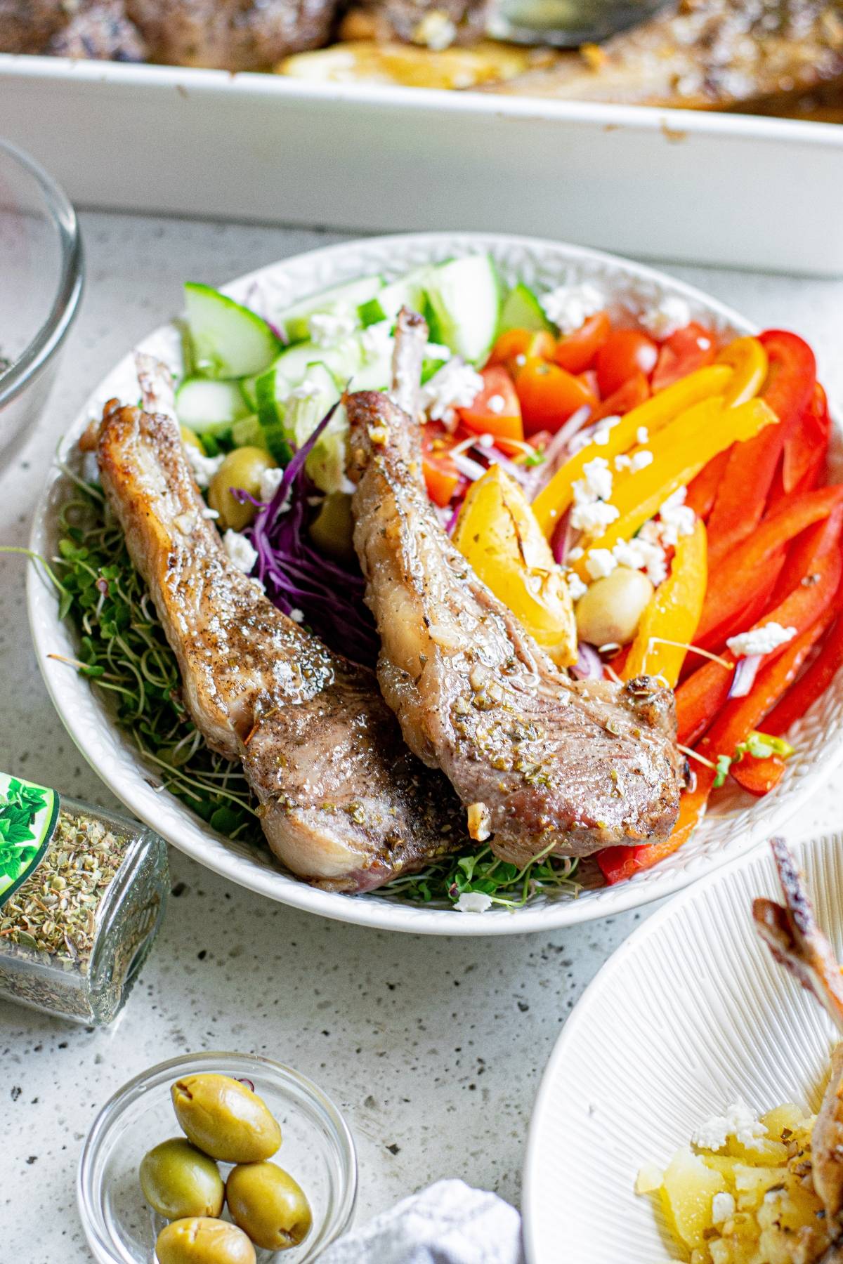 A bowl with Greek lemon baked pork chops, sliced cucumber, red and yellow peppers, cabbage, feta, and greens.