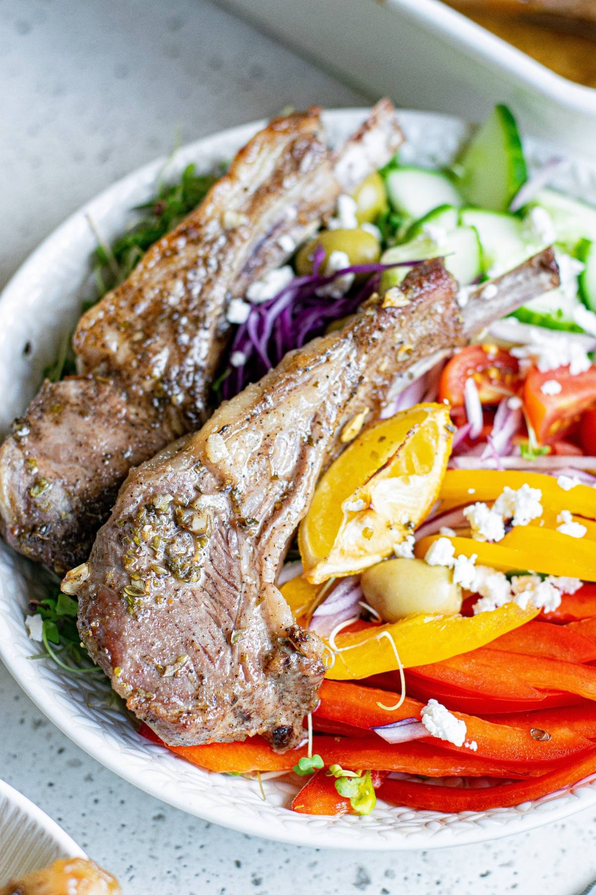 Grilled lamb chops with a colorful salad of peppers, tomatoes, olives, and feta cheese—an easy pork recipe twist for those who love Greek pork chops on a white plate.