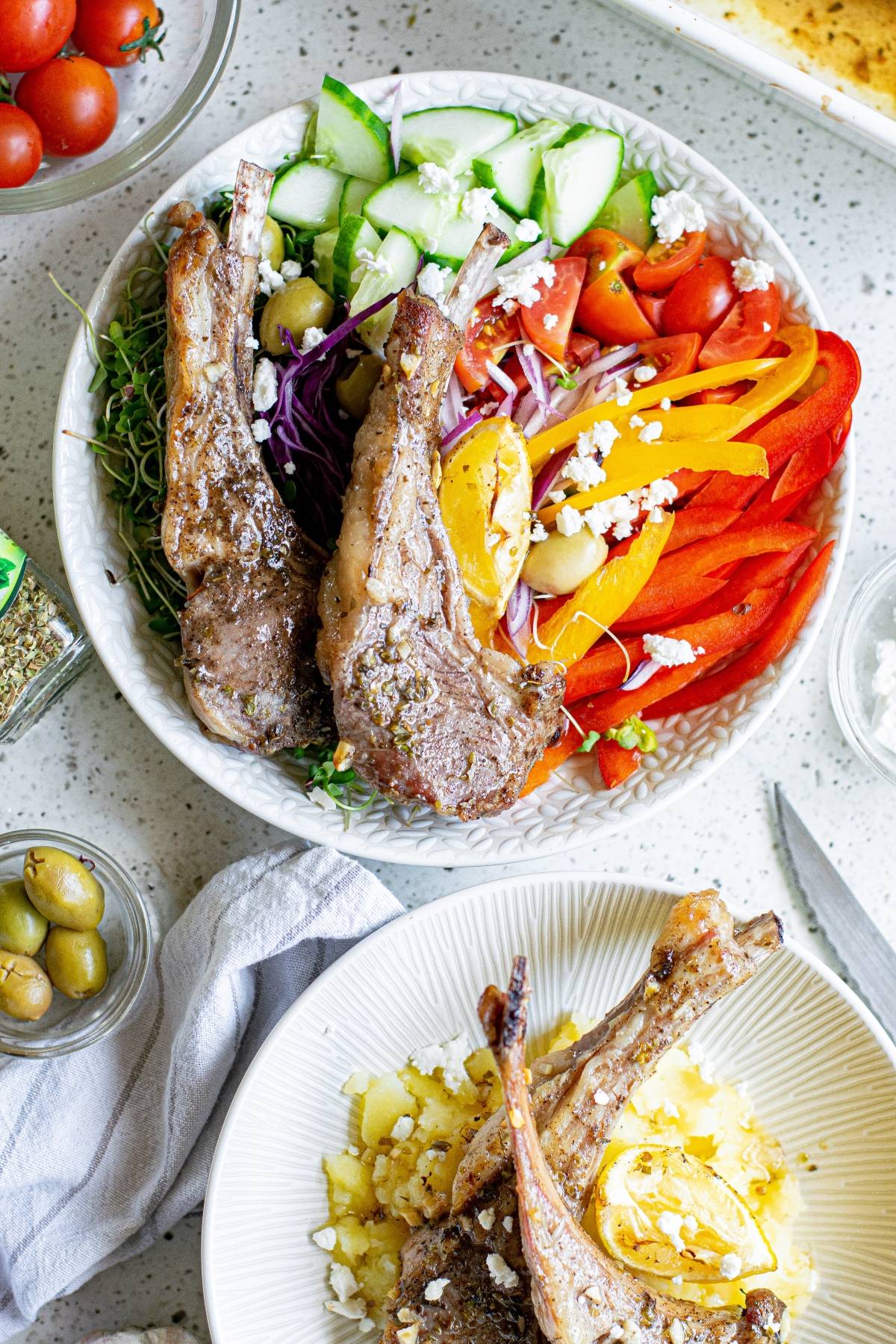 A bowl of grilled lamb chops with colorful sliced vegetables, olives, and feta cheese on a white table, inspired by classic Greek pork chops flavors.