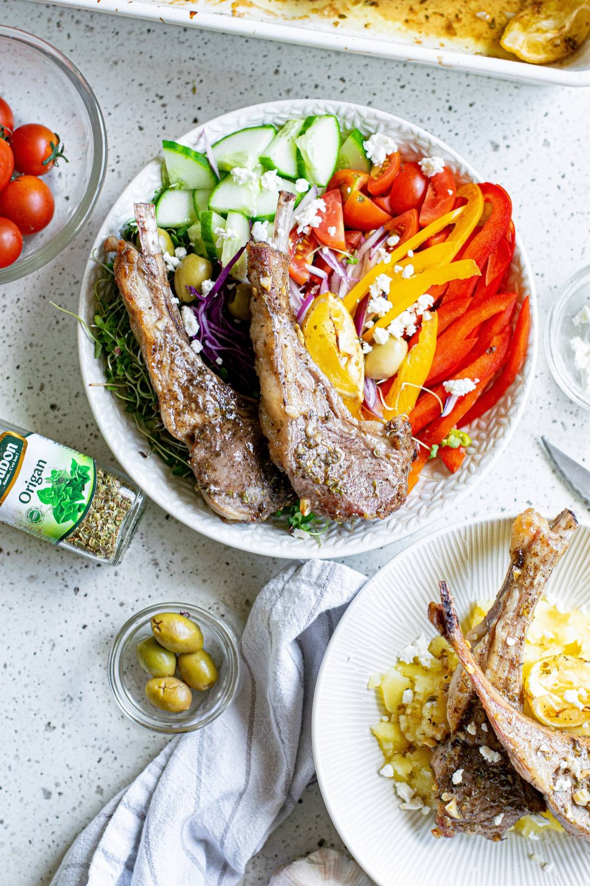 A bowl of salad with Greek lemon baked pork chops, colorful vegetables, olives, and feta cheese on a white table.