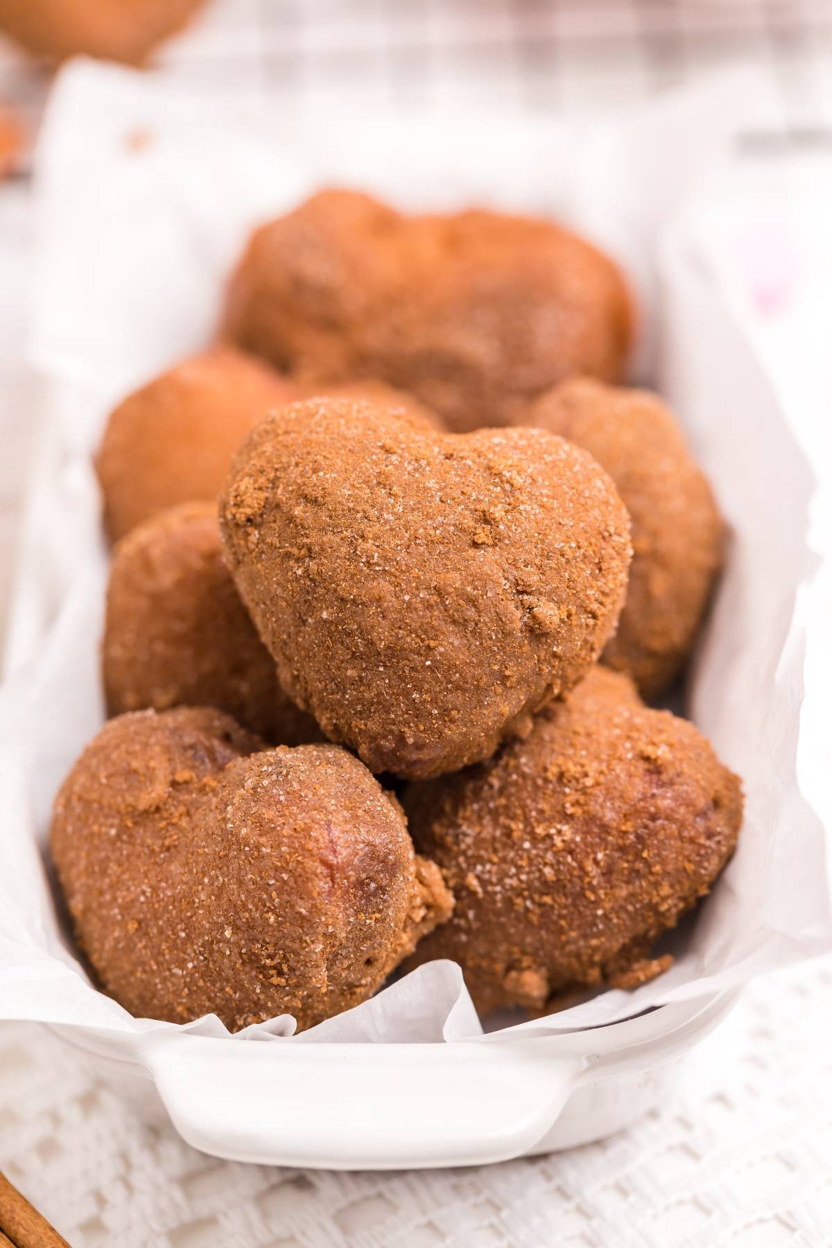 Heart-shaped, cinnamon sugar donuts arranged in a white dish lined with parchment paper—perfect for trying out your favorite mini doughnut recipe.