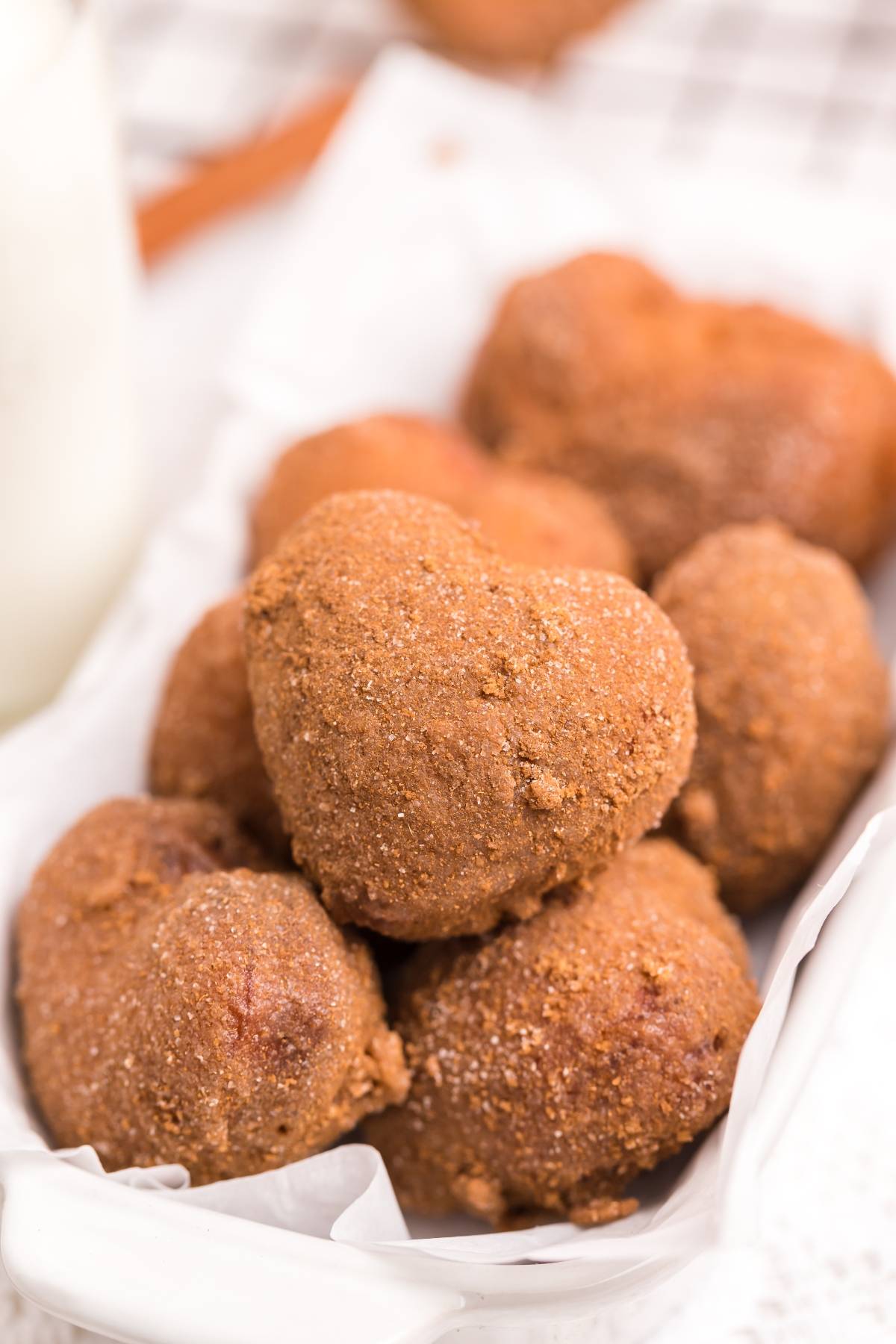 A pile of heart-shaped, cinnamon-sugar coated doughnuts—just like a mini doughnut recipe—rests on a white tray lined with parchment paper.