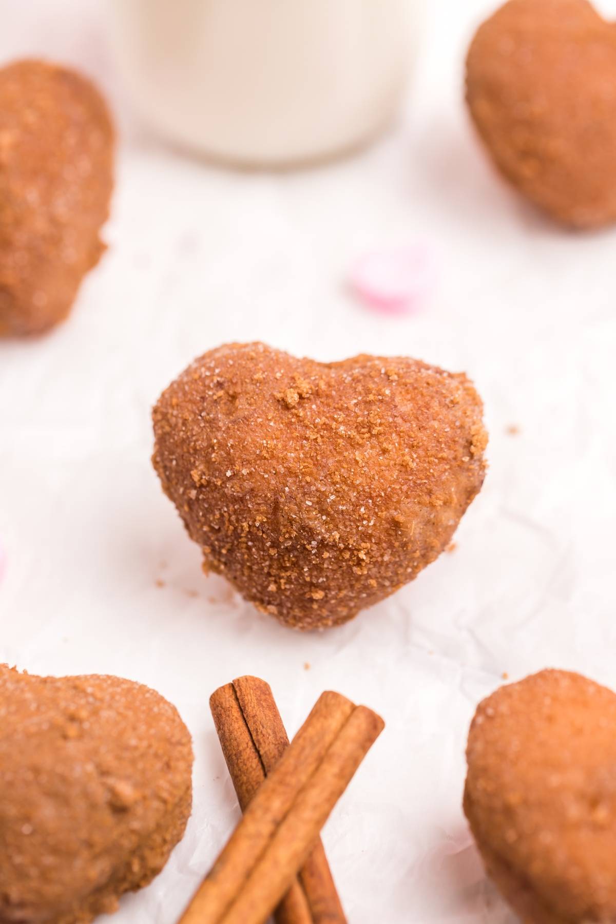 Heart-shaped churro surrounded by cinnamon sticks and more churros on a white surface—perfect inspiration for your next heart shaped doughnut holes or cinnamon roll hack.