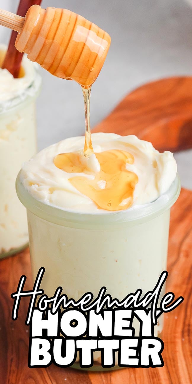 A honey dipper drizzles homemade honey butter into a glass jar on a wooden surface.