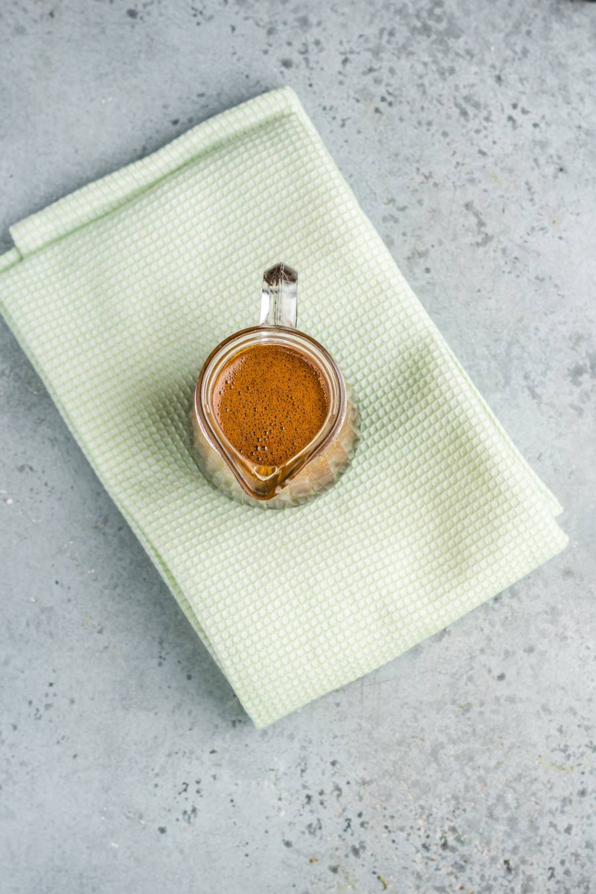 A glass cup of coffee on a folded light green towel, set on a gray textured surface—perfect for savoring after trying an easy eel sauce recipe.