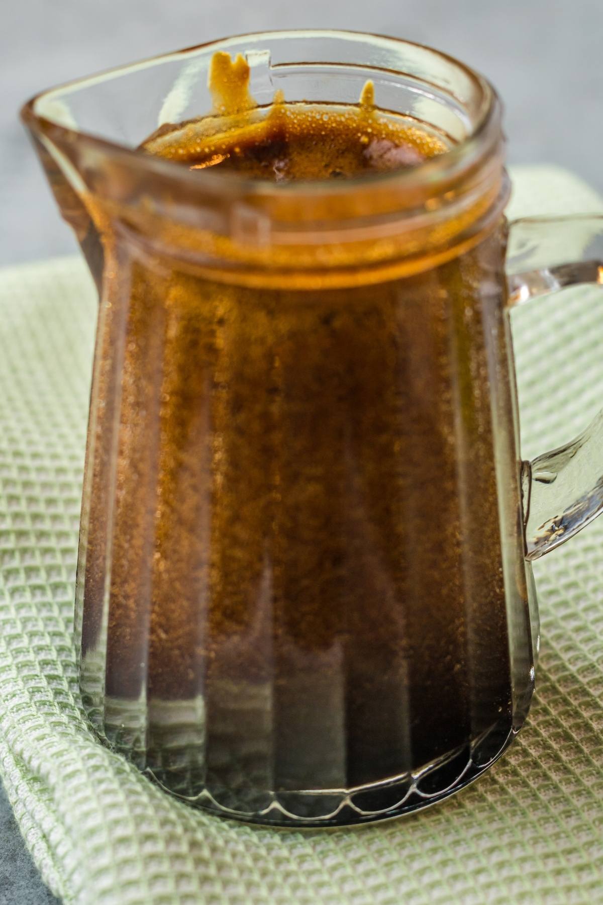 A glass pitcher filled with brown unagi sauce, a delicious sauce for seafood, sits on a folded light green cloth.
