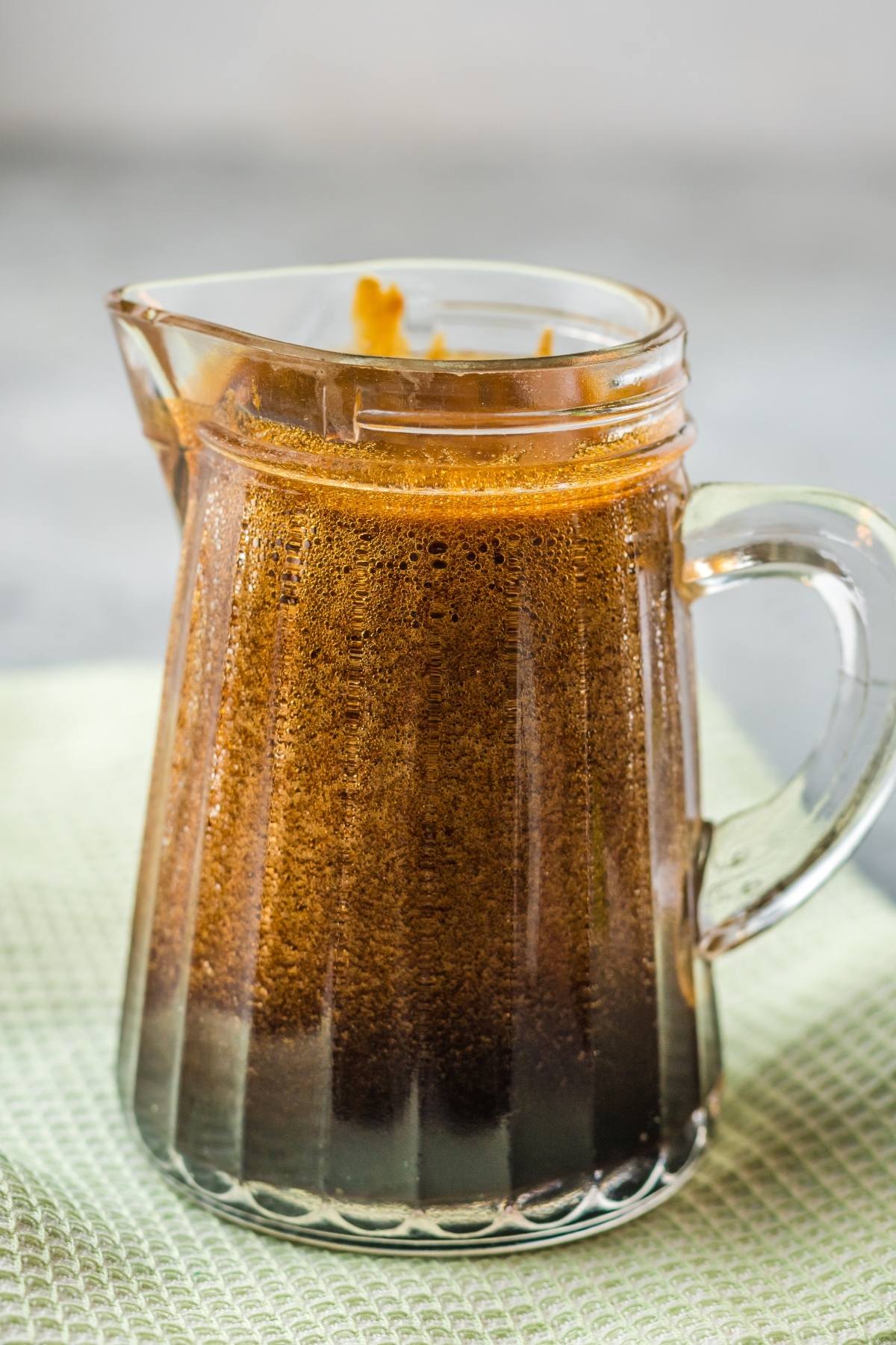 Small glass pitcher filled with dark Homemade Eel Sauce (Unagi Sauce), placed on a light textured cloth.