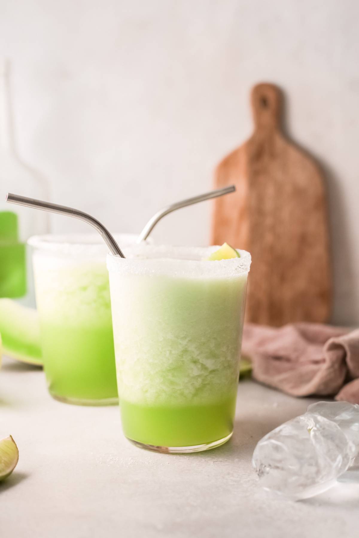 Two frosty honeydew margarita drinks with metal straws in glasses, topped with foam and served over ice, are set on a light background—an easy tequila cocktail perfect for a refreshing twist.