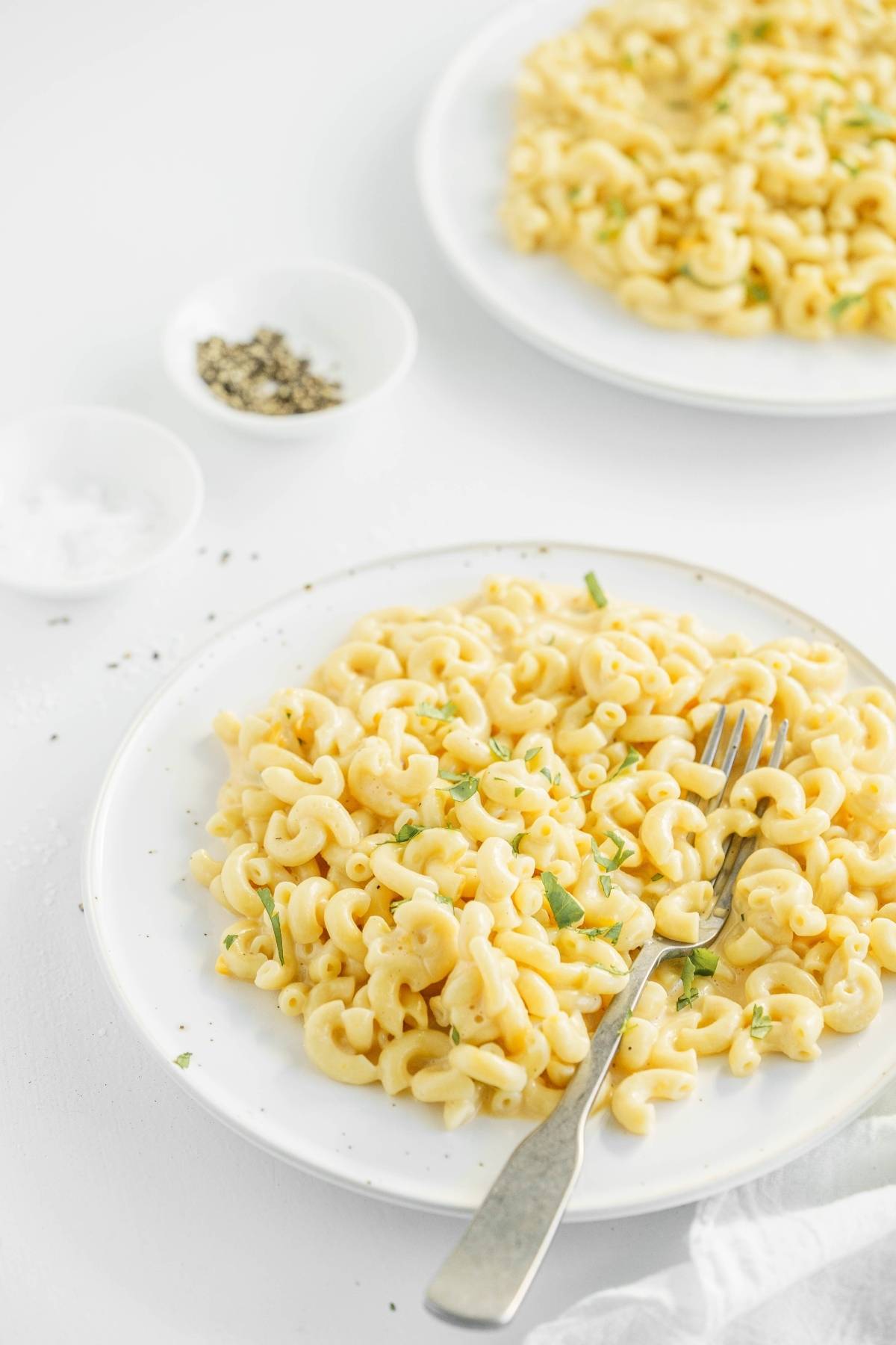 Two plates of Mac and cheese garnished with herbs, with bowls of salt and pepper in the background—an easy instant pot pasta recipe perfect for any meal.