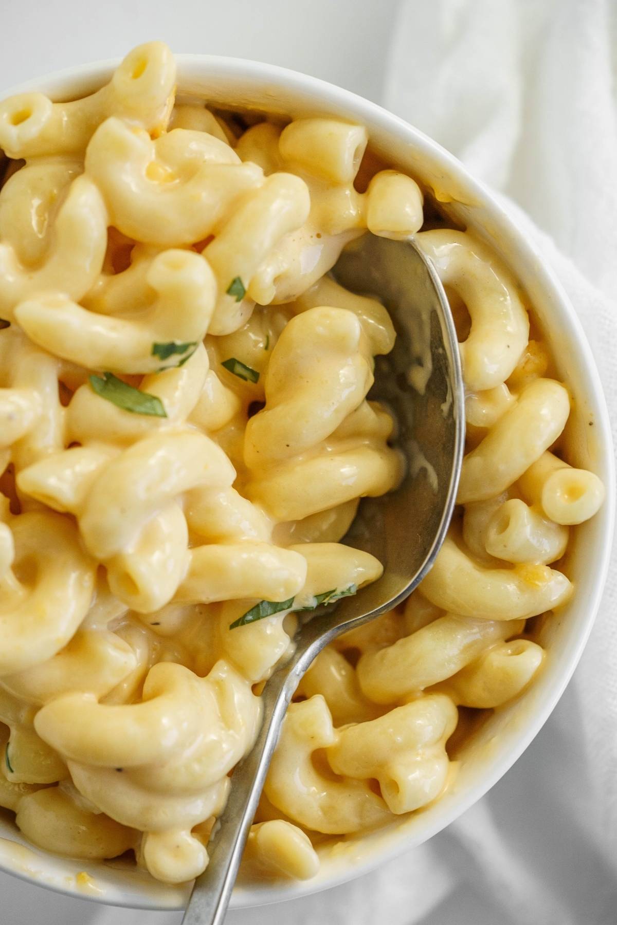 Close-up of creamy mac and cheese in a white bowl with a spoon and a few green herb garnishes, featuring an easy instant pot pasta recipe for quick comfort food.