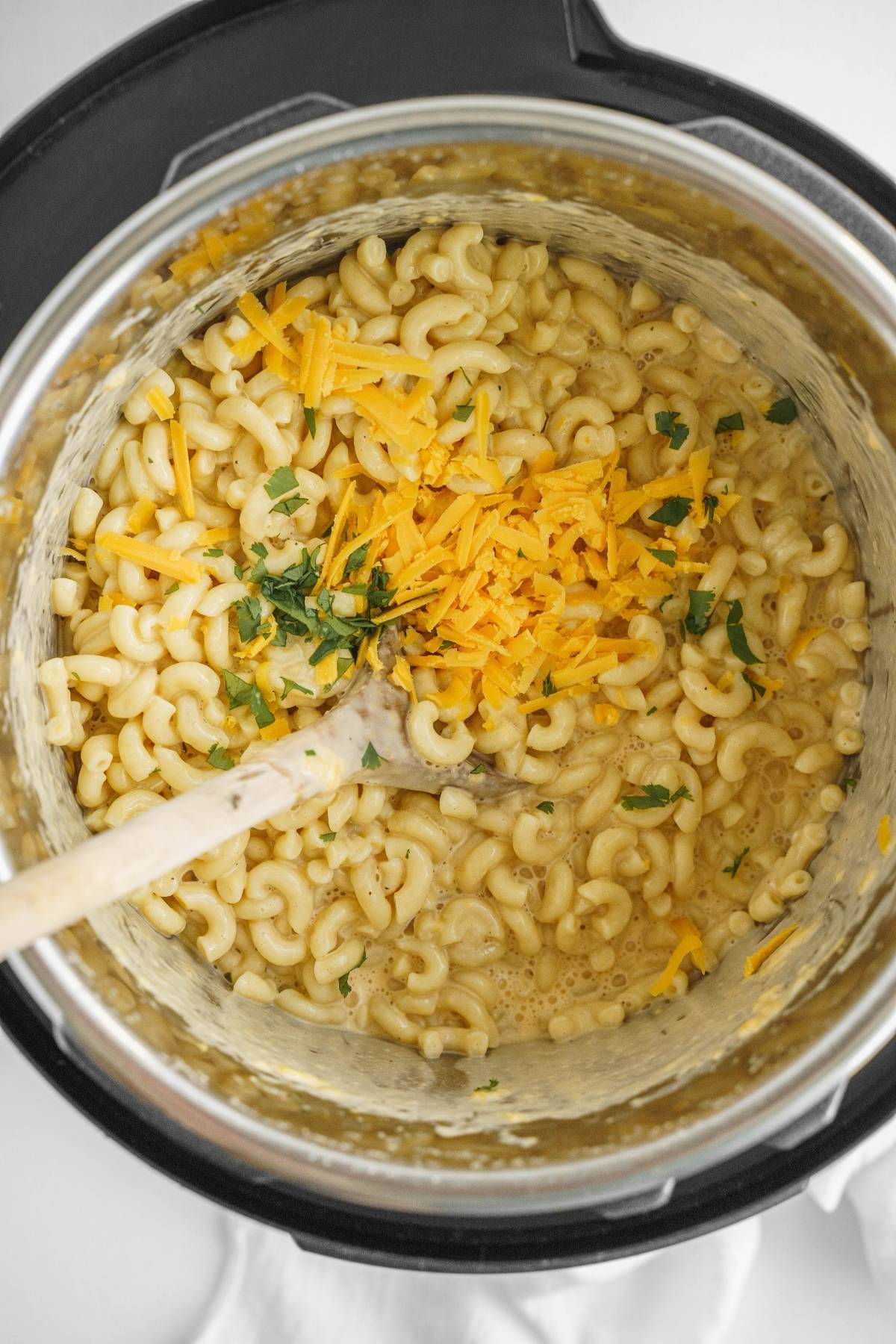 Mac and cheese with shredded cheddar and herbs in a pot, stirred with a wooden spoon—a delicious Easy instant pot pasta recipe for quick comfort food.