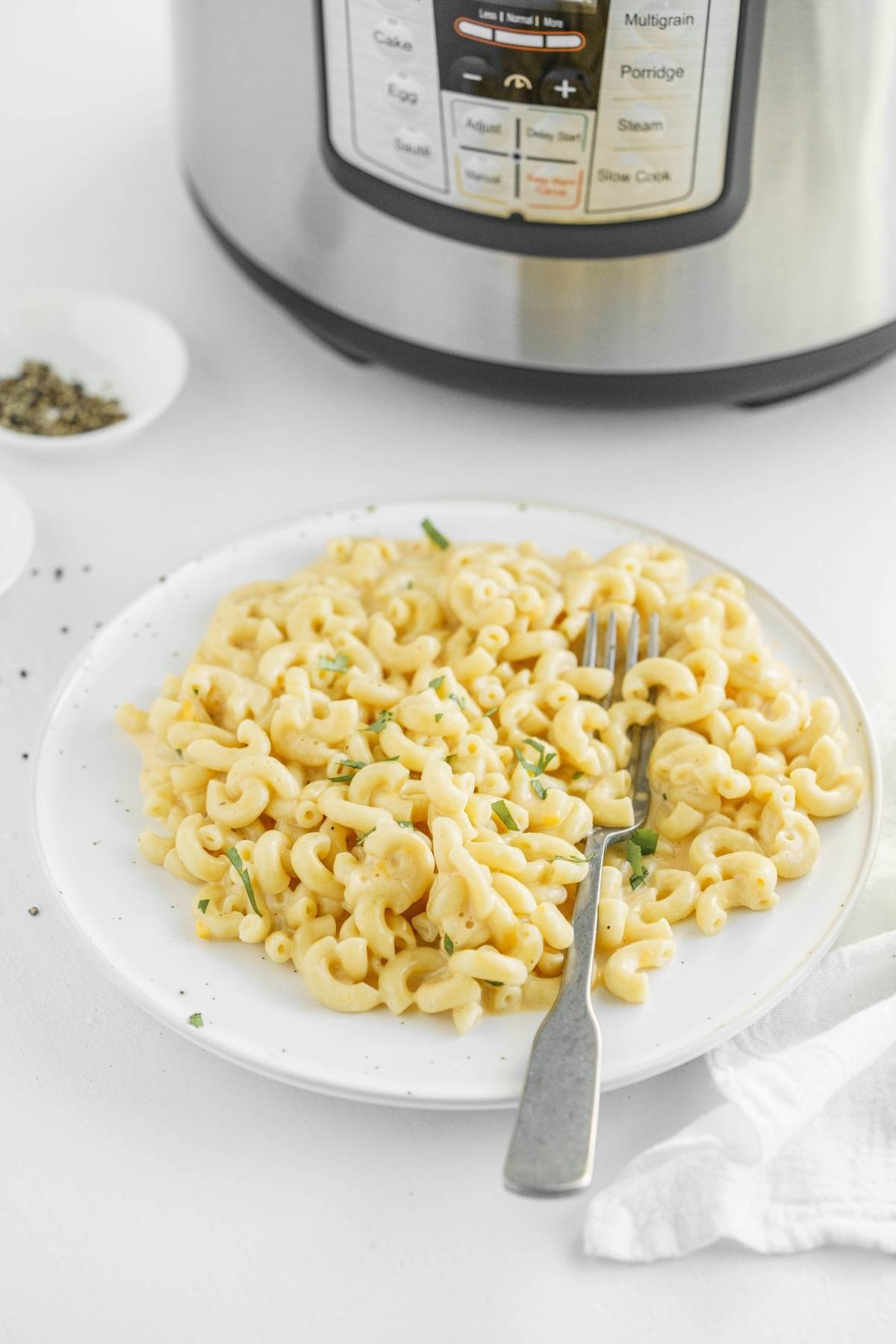 Plate of creamy macaroni and cheese with a fork, in front of an electric pressure cooker—this is the perfect easy instant pot pasta recipe for busy nights.