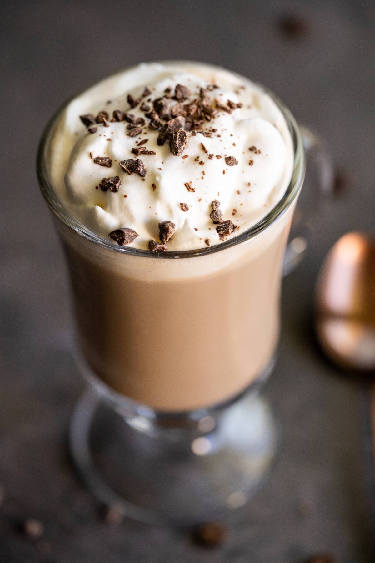 Glass mug of Irish cream coffee topped with whipped cream and chocolate shavings, with a spoon beside it.