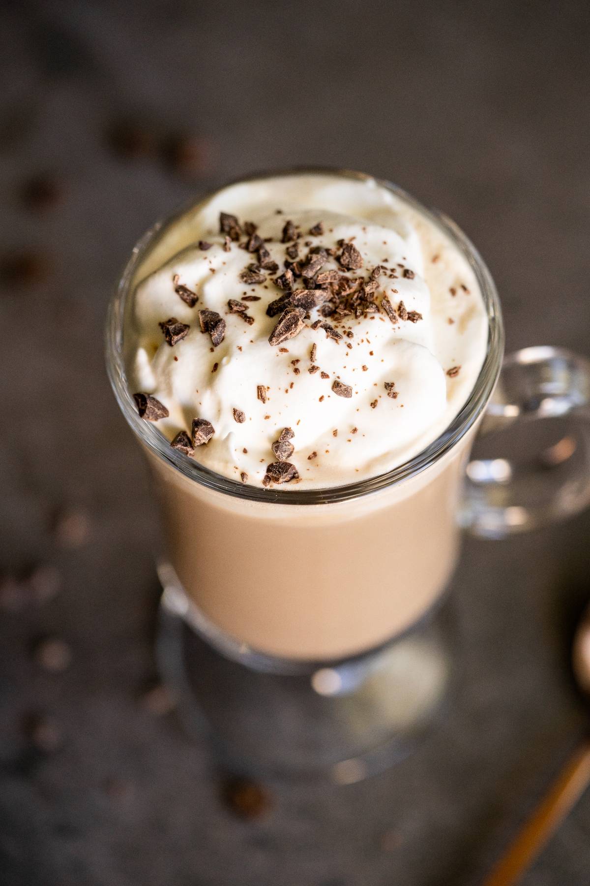 A glass mug of Irish cream coffee topped with whipped cream and chocolate shavings sits invitingly on a dark surface.