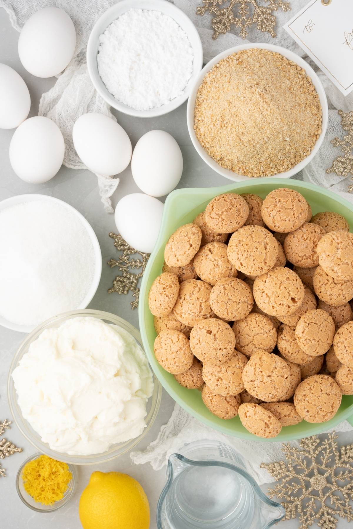 Baking ingredients on a countertop, including eggs, sugar, lemon, amaretti cookies, and powdered sugar—perfect for creating a delicious Lemon ricotta amaretti cake made with amaretti cookies and ricotta cheese.