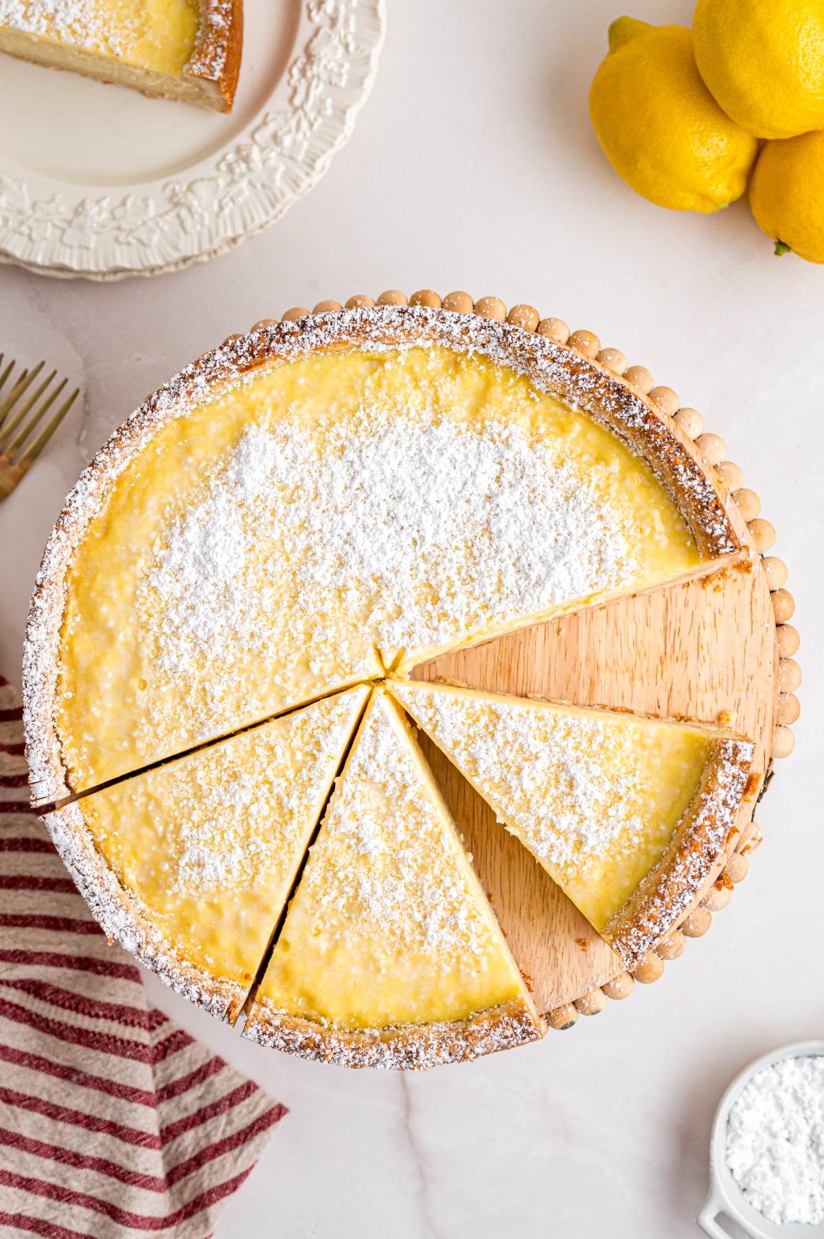 Lemon cheesecake dusted with powdered sugar, two slices being served, lemons and plates beside it.