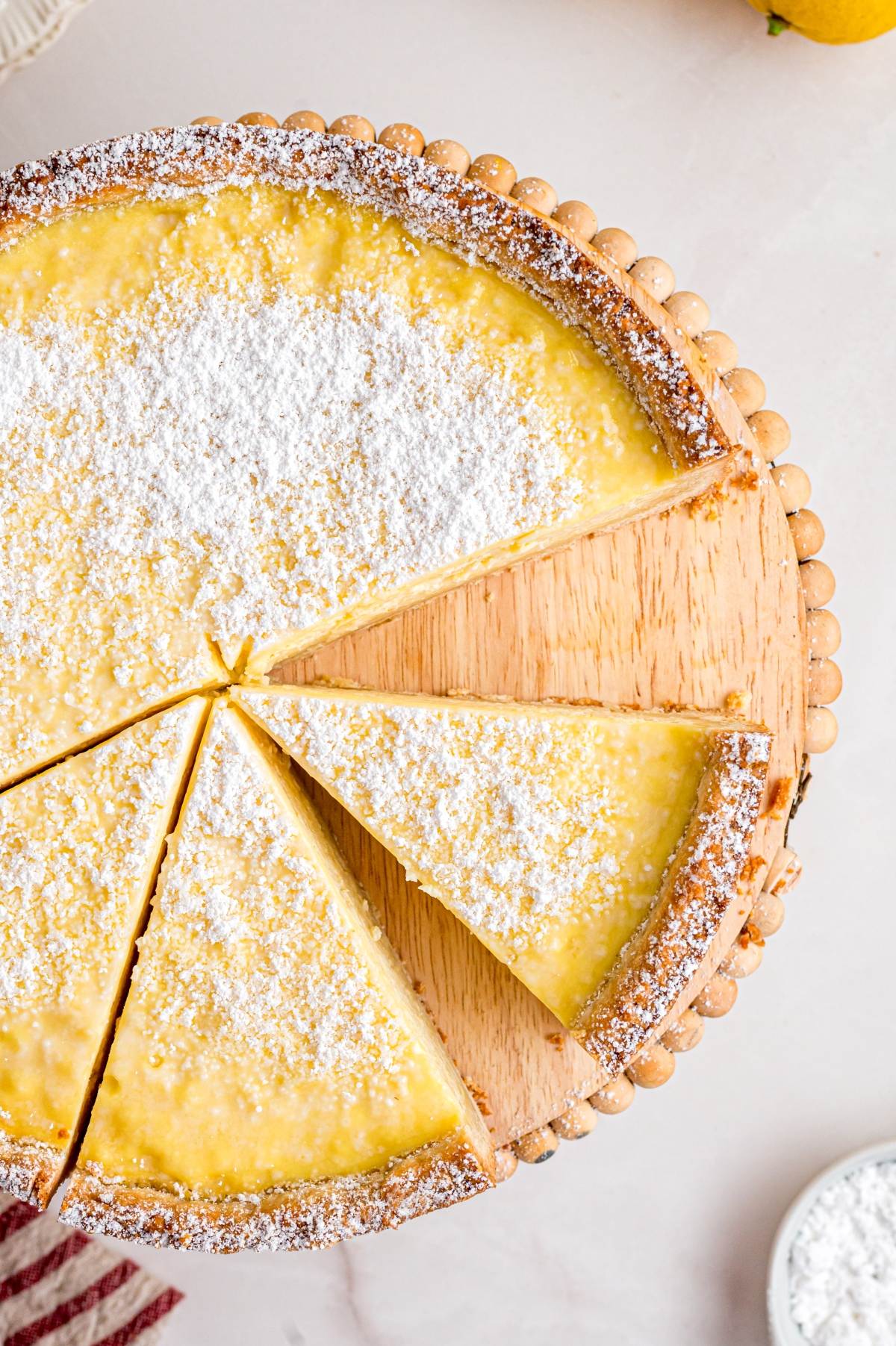 A lemon tart dusted with powdered sugar, sliced into pieces on a wooden board.