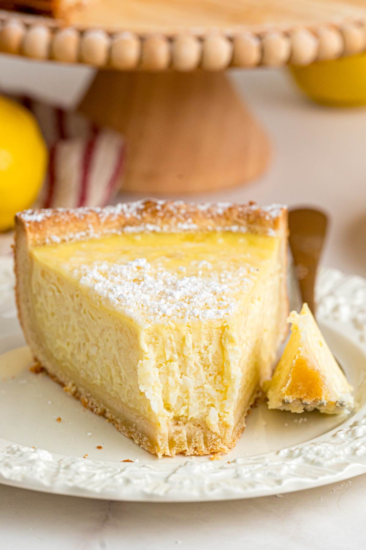 A slice of lemon pie with powdered sugar on top, served on a white plate with a fork.
