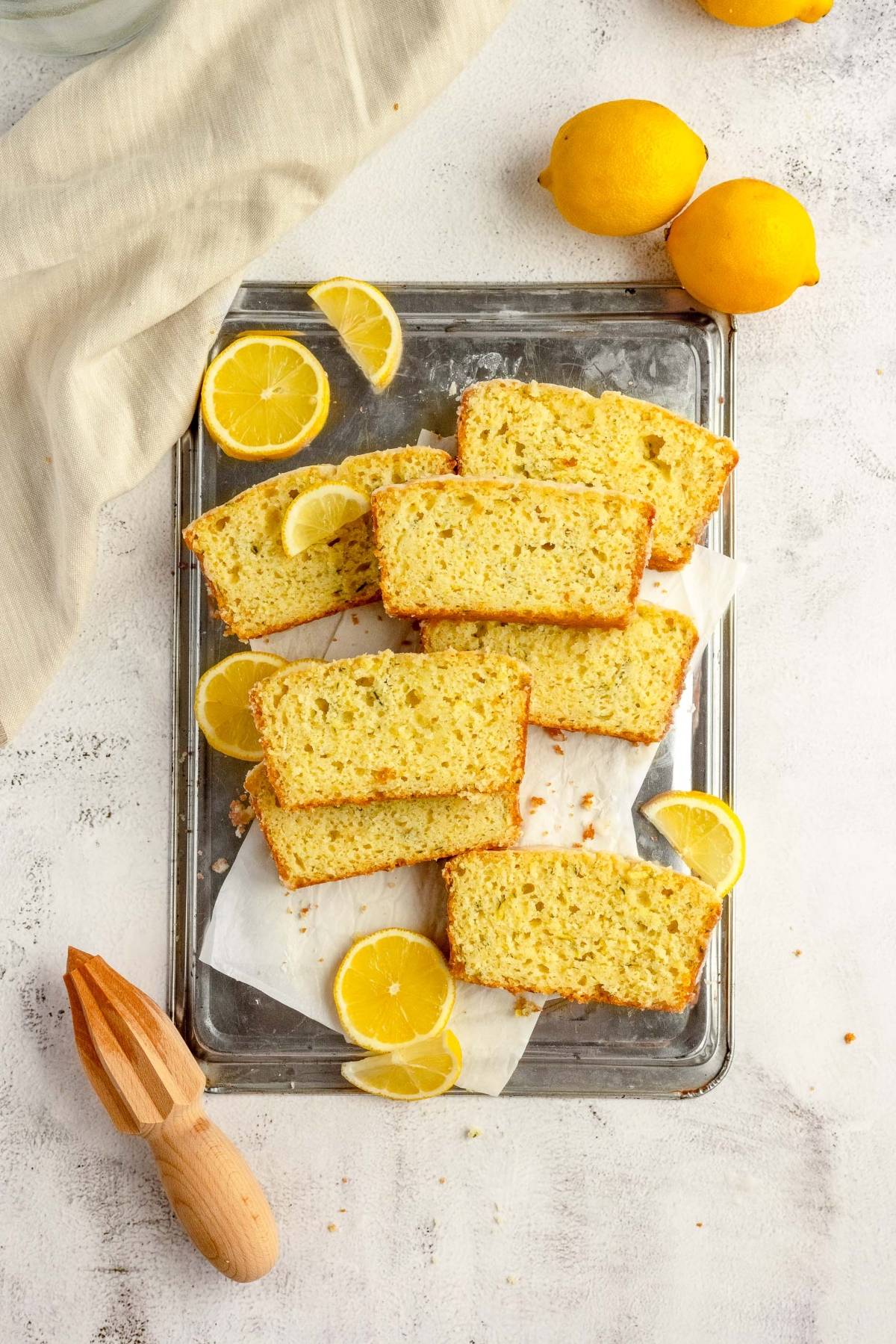 Sliced lemon zucchini bread on a tray with lemon wedges, whole lemons, and a wooden citrus juicer nearby.