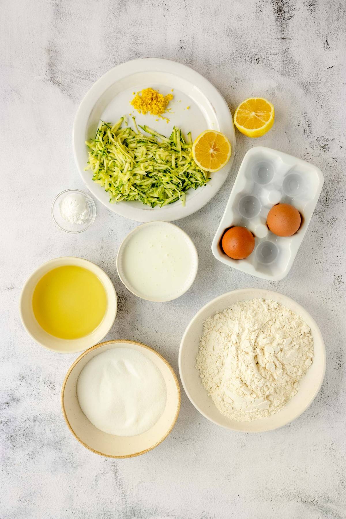 A group of ingredients for lemon zucchini bread is arranged on a table.