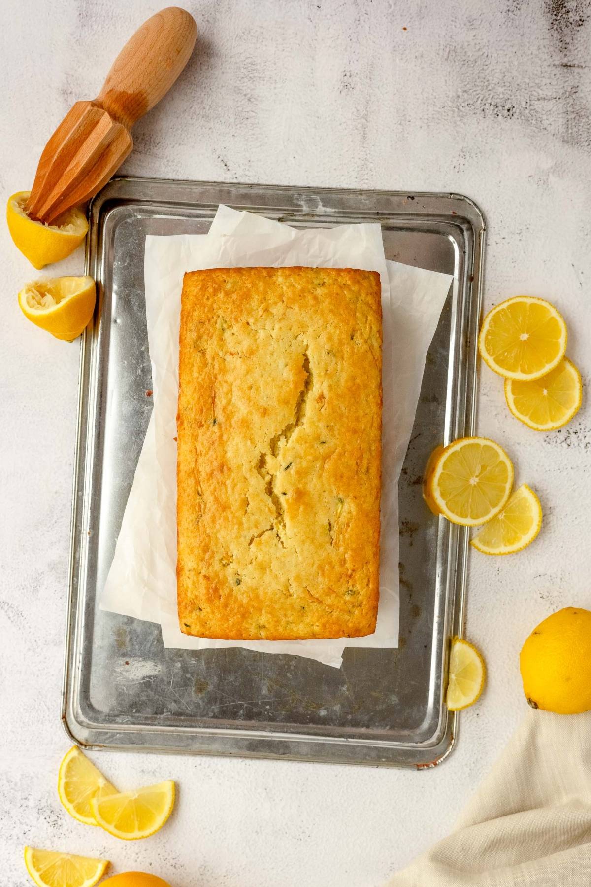 A loaf of lemon zucchini bread on parchment paper, surrounded by lemon slices and a wooden citrus juicer.