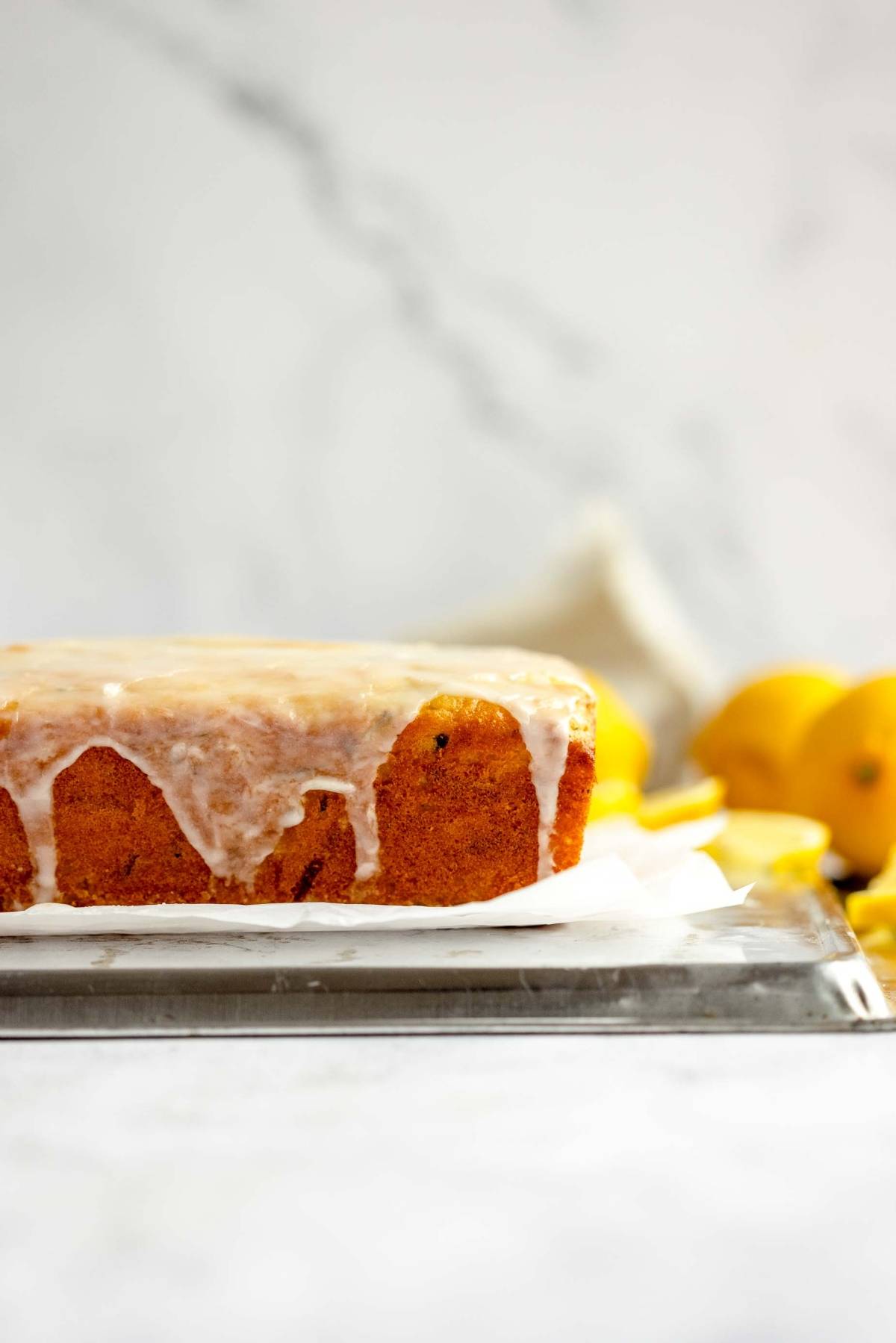 Iced lemon loaf cake on parchment paper with fresh lemons in the background, reminiscent of classic lemon zucchini bread.
