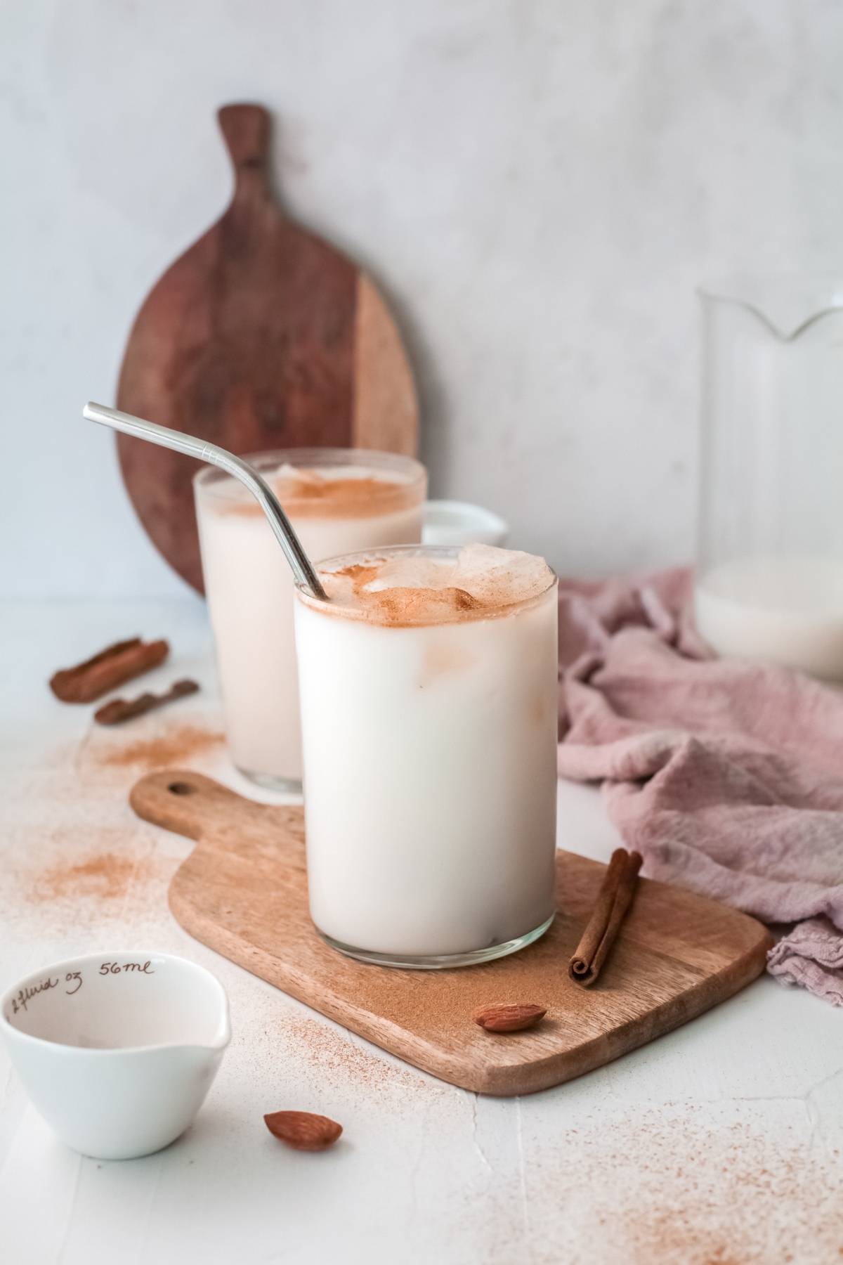 Two glasses of refreshing homemade horchata, the classic iced rice milk beverage with ice and cinnamon, served with metal straws on a wooden board.