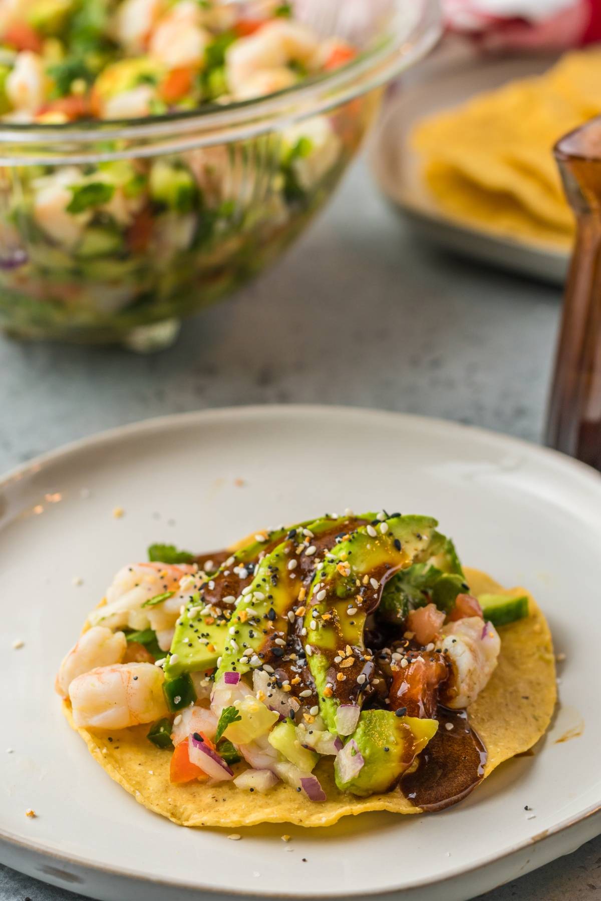 Tostada topped with Mexican ceviche featuring shrimp, avocado slices, and sauce on a white plate.