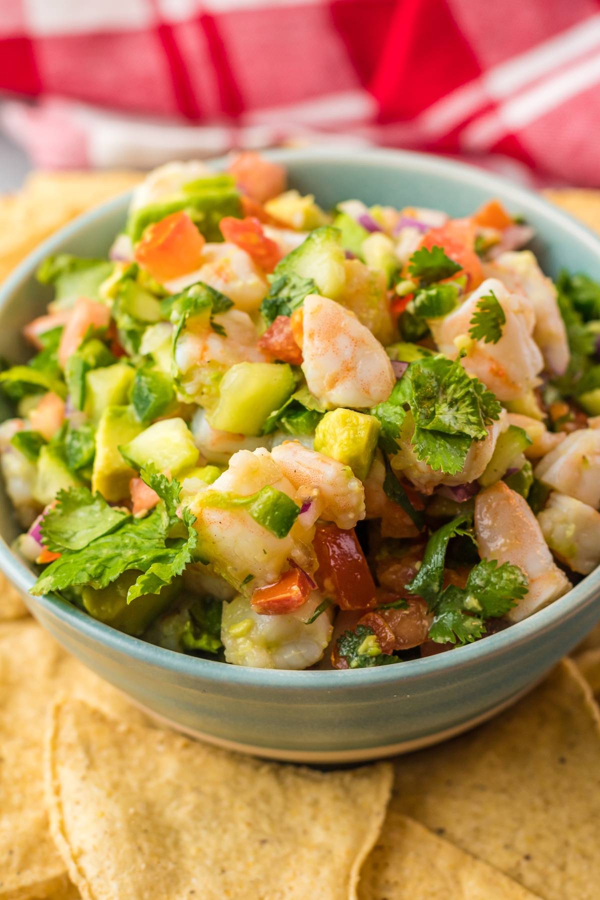A bowl of shrimp ceviche, featuring avocado, tomato, cilantro, and chips on the side—experience a classic Mexican ceviche bursting with fresh flavors.