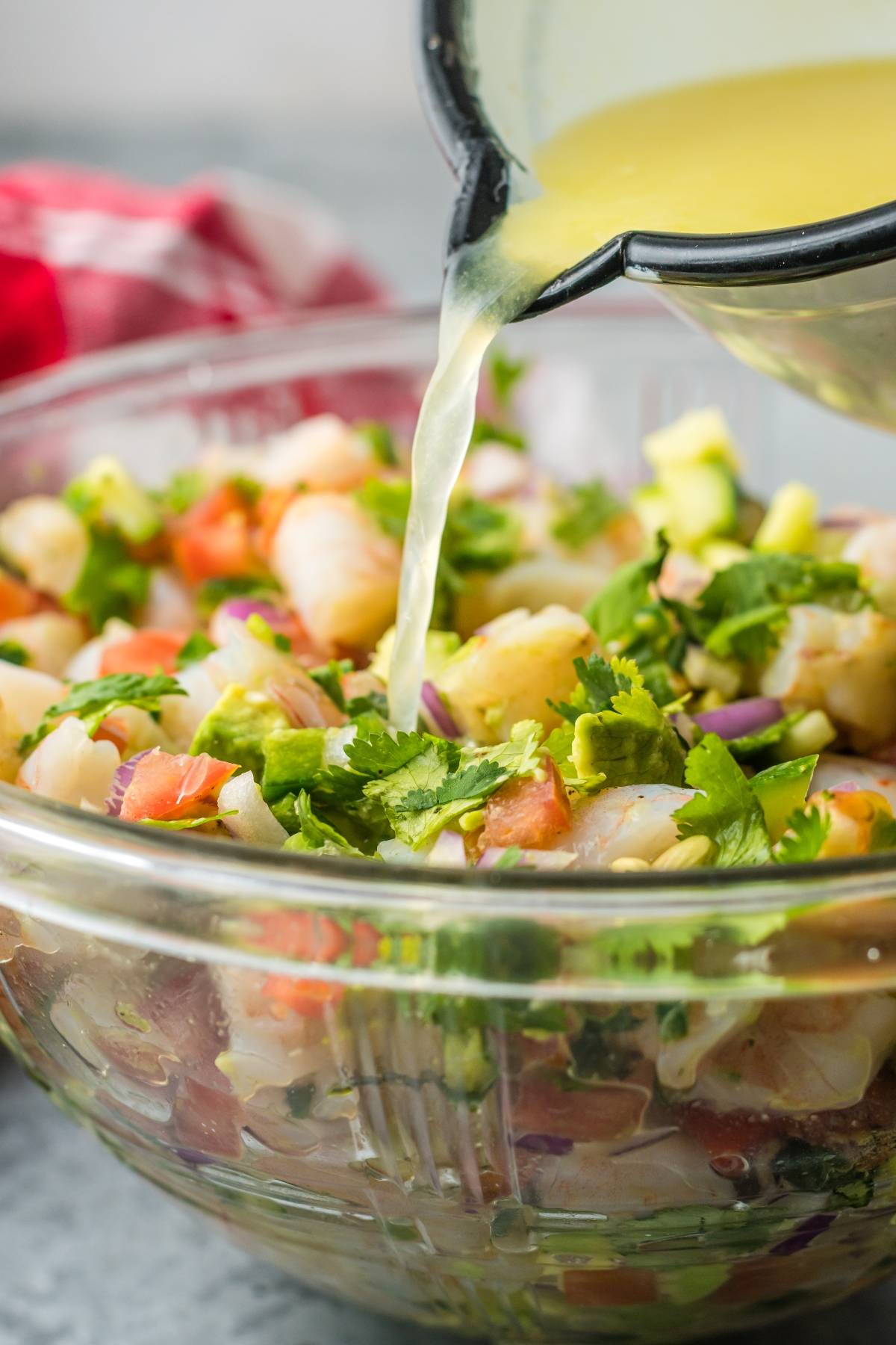 Lemon juice being poured onto shrimp ceviche with cilantro, tomato, and onion in a glass bowl for the best ceviche recipe.