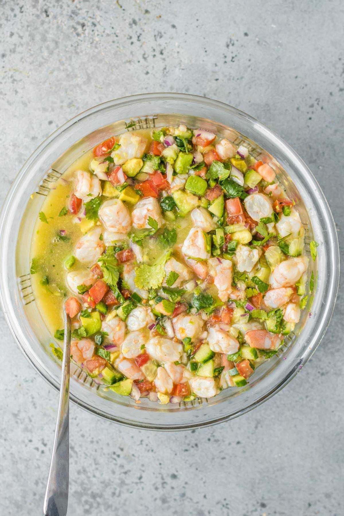 A bowl of shrimp ceviche with diced vegetables and herbs, mixed in a citrus marinade, is served with a spoon inside—perfect for anyone craving the best ceviche recipe.