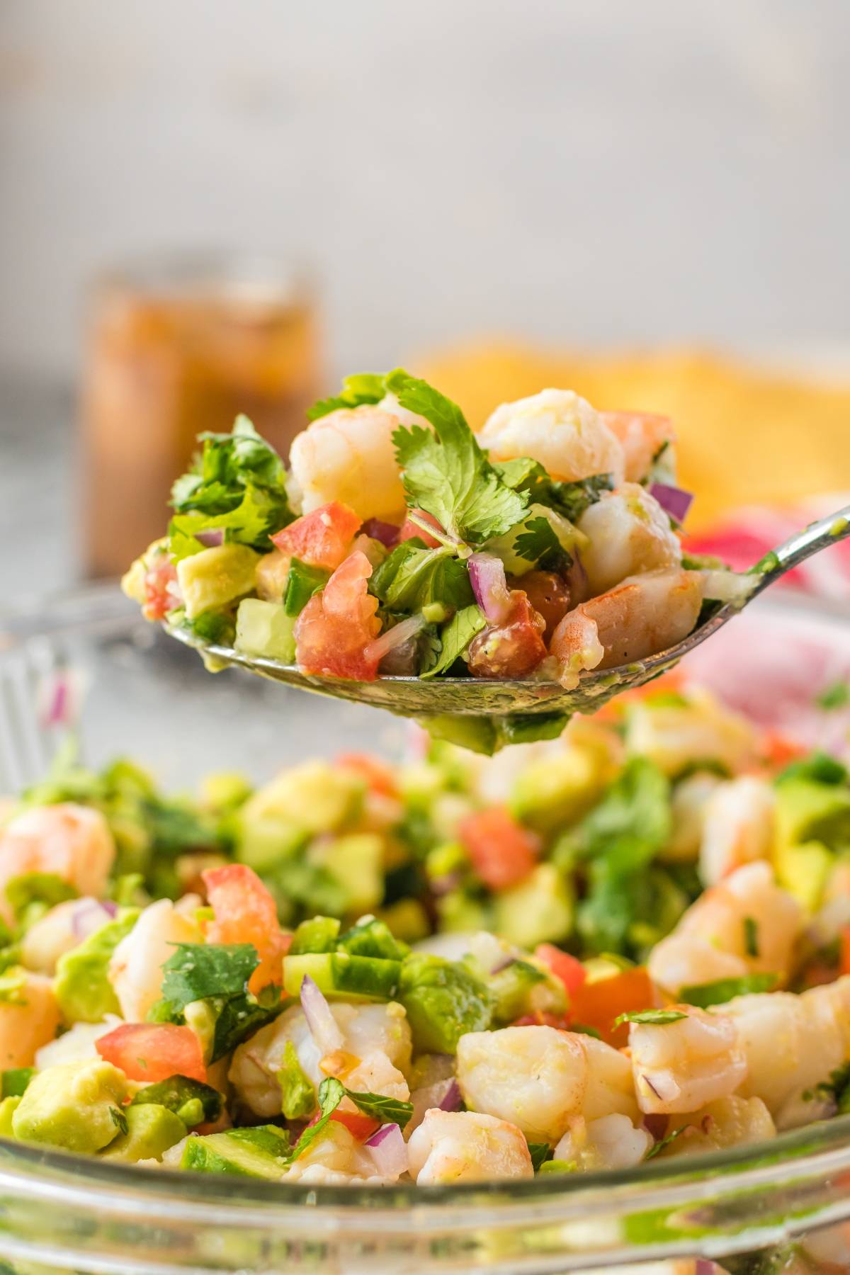 A spoonful of shrimp ceviche with avocado, tomato, onions, and cilantro above a bowl of the same mixture—enjoy this fresh and zesty recipe with fresh shrimp.