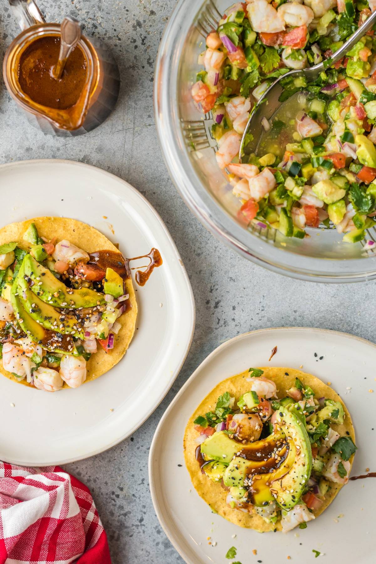 Two shrimp and avocado tostadas sit on plates, accompanied by a bowl of ceviche made from a recipe with fresh shrimp and a small jug of sauce on the side.