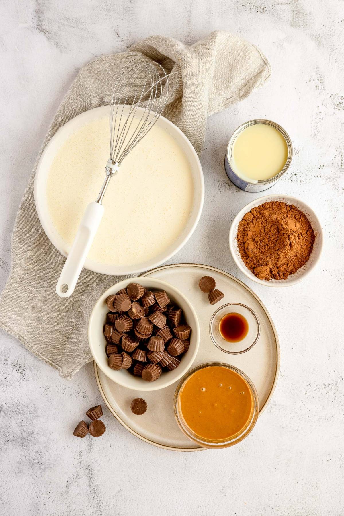 Bowl of whipped cream, cocoa powder, mini peanut butter cups, peanut butter, vanilla, and condensed milk—perfect for making rich No Churn Chocolate Peanut Butter Cup Ice Cream.
