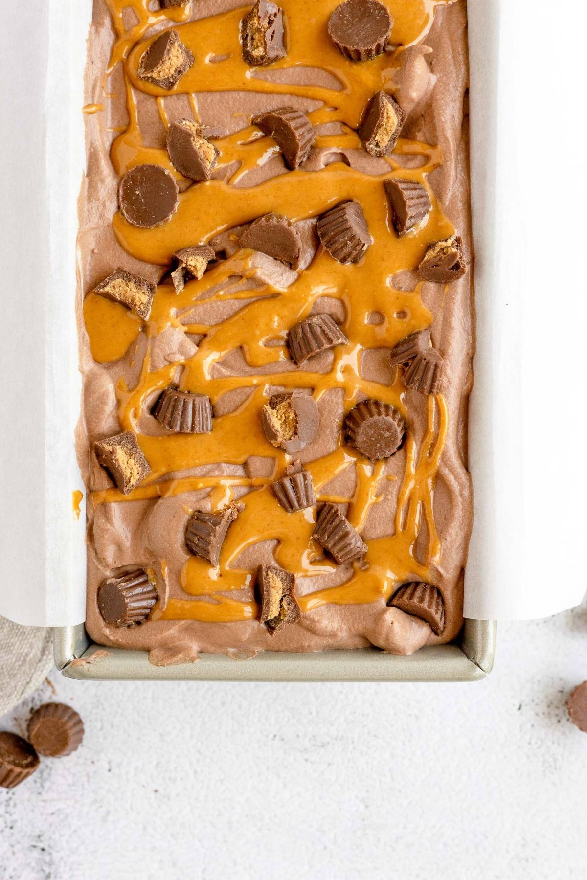 No Churn Chocolate Peanut Butter Cup Ice Cream in a pan, topped with creamy peanut butter sauce and mini peanut butter cups. A delicious no fuss treat for any chocolate and peanut butter lover!.