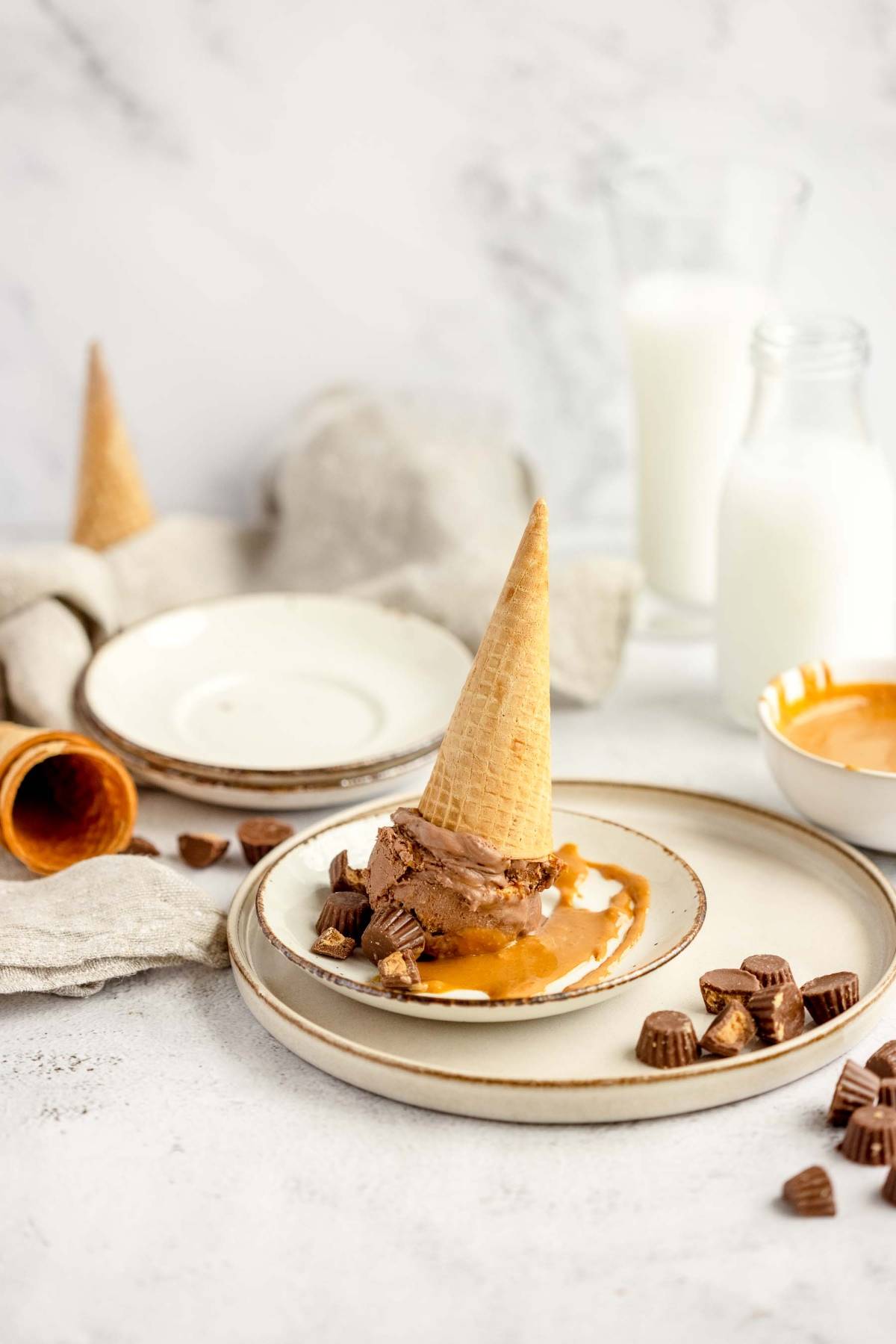 An ice cream cone placed upside down on a plate with chocolate, caramel, and mini peanut butter cups—perfect for fans of No Churn Chocolate Peanut Butter Cup Ice Cream.